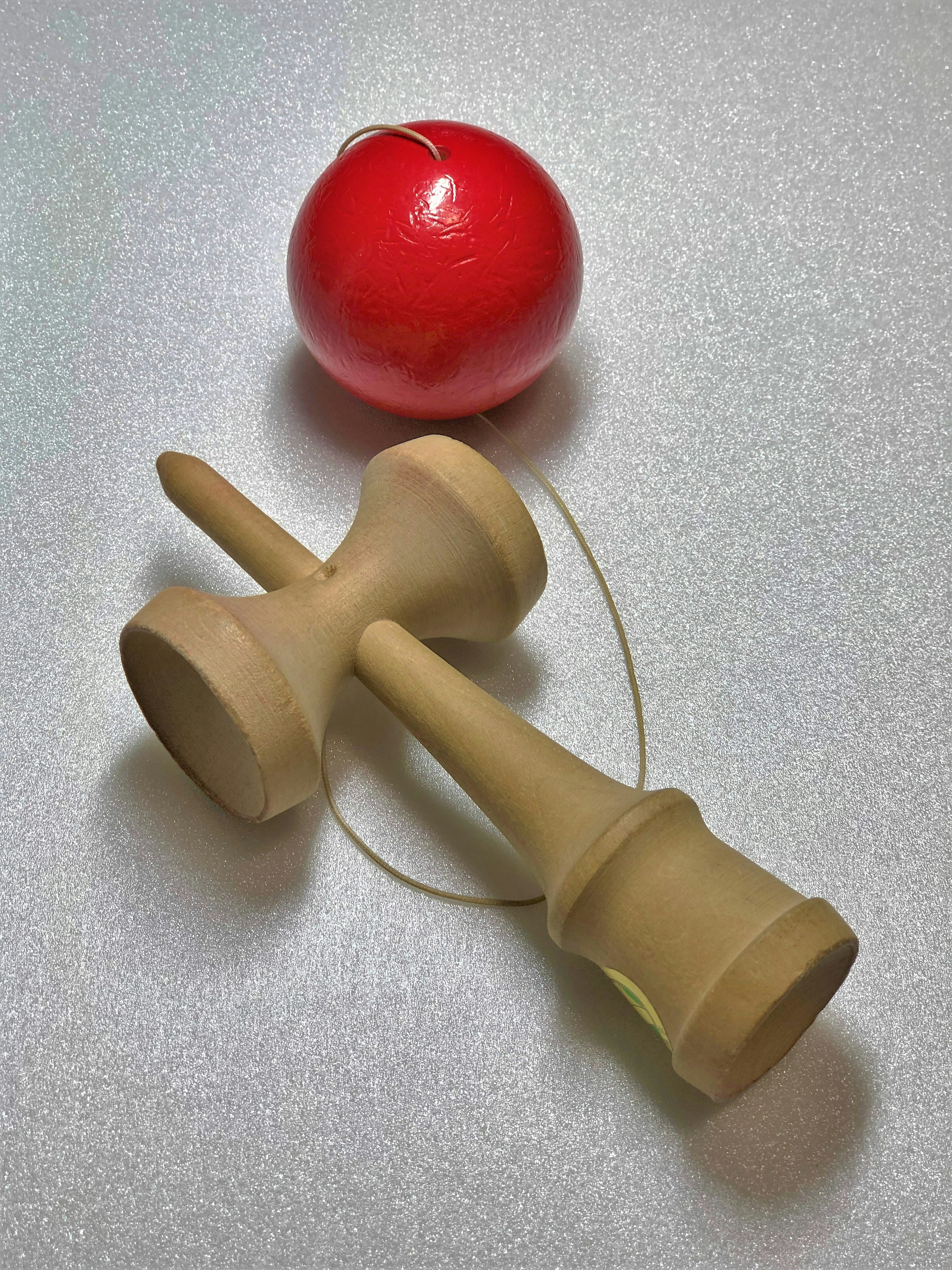 A kendama toy featuring a red ball and wooden handles