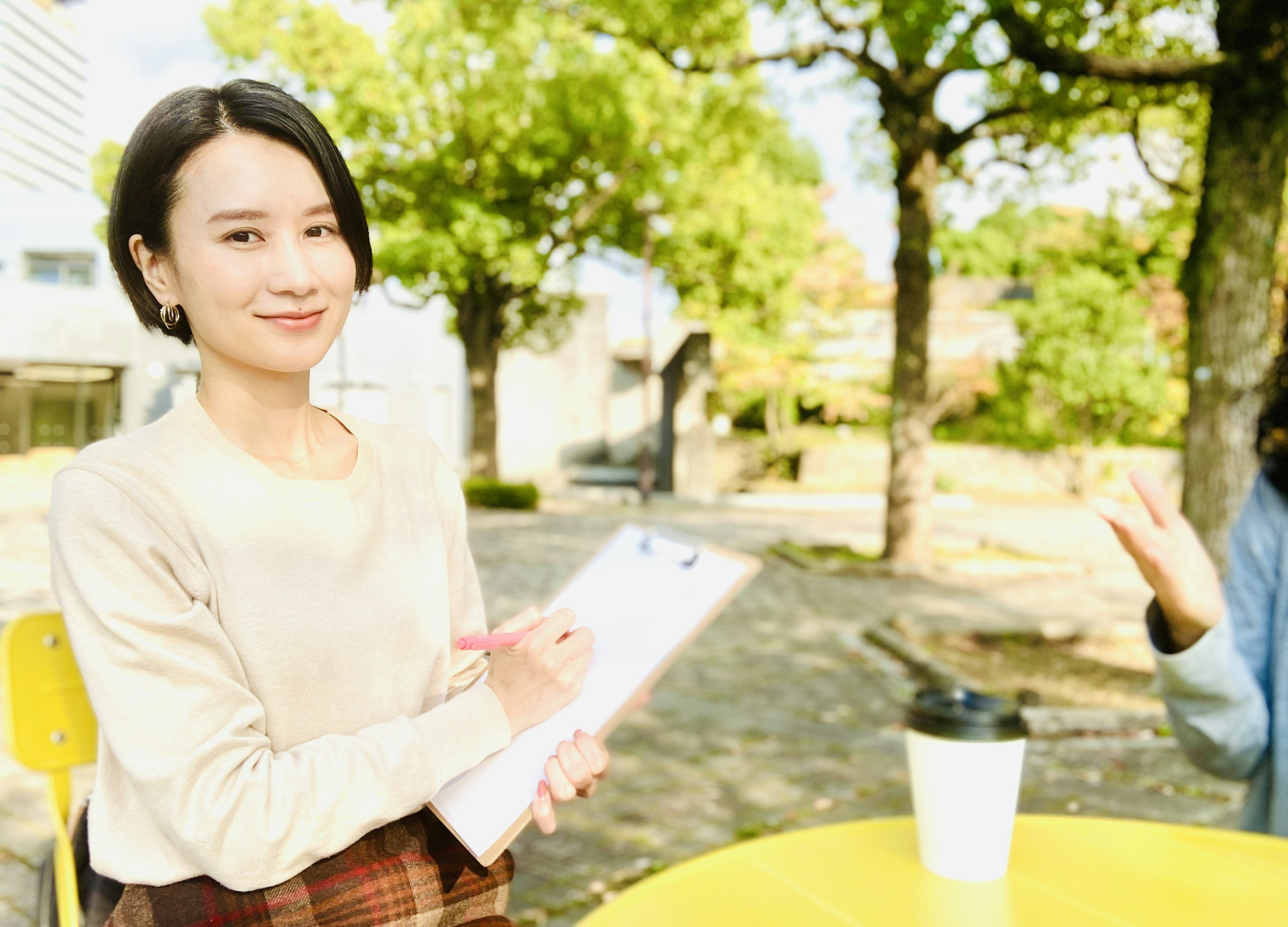 在公园被采访的女性，周围是绿色的树木和明亮的阳光