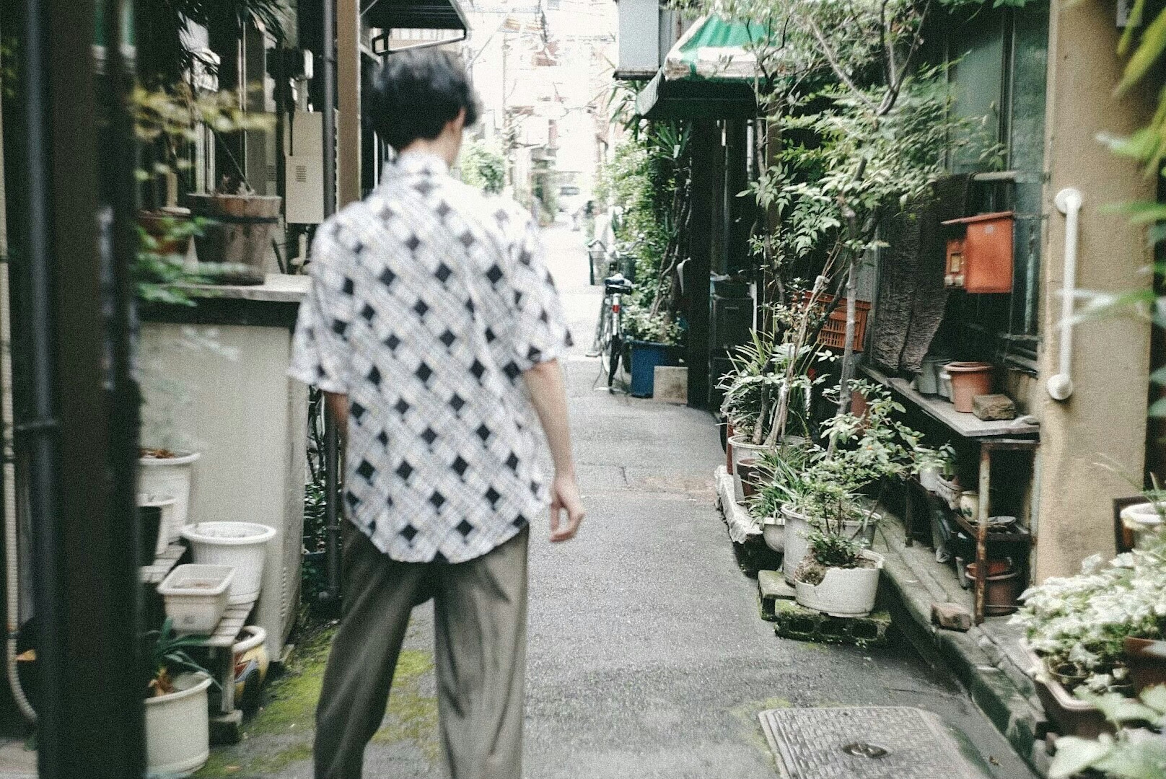 A man walking down a narrow alley surrounded by plants and flowers