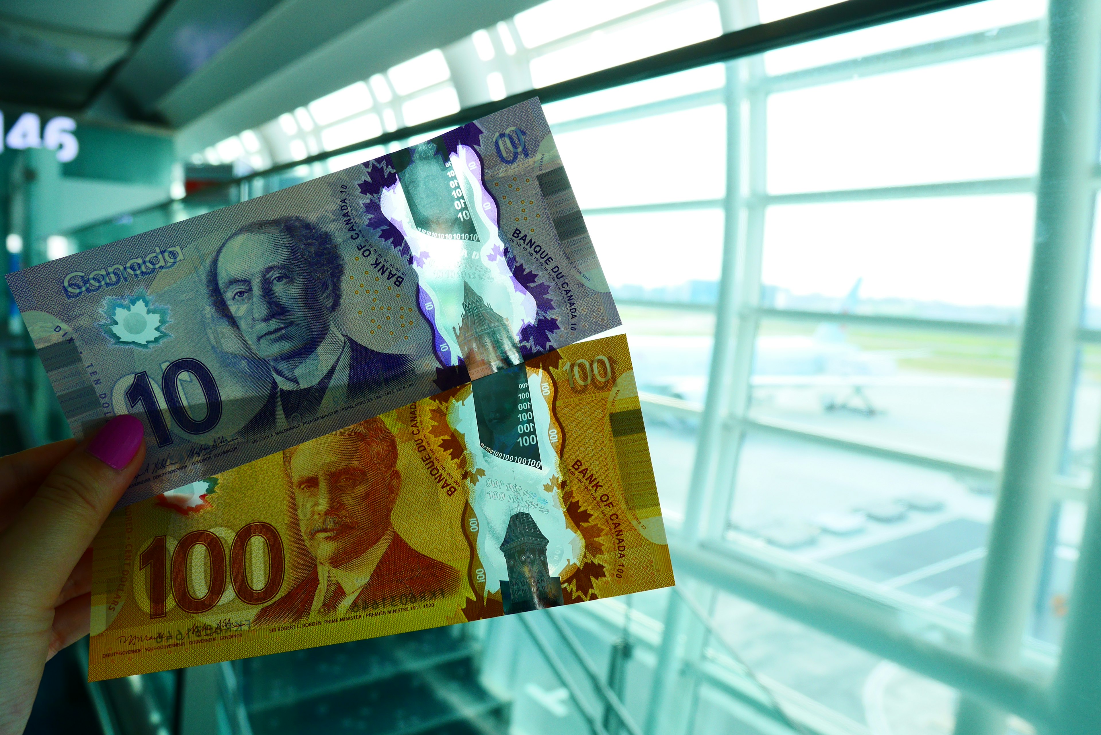 A hand holding two banknotes in an airport setting with a view outside