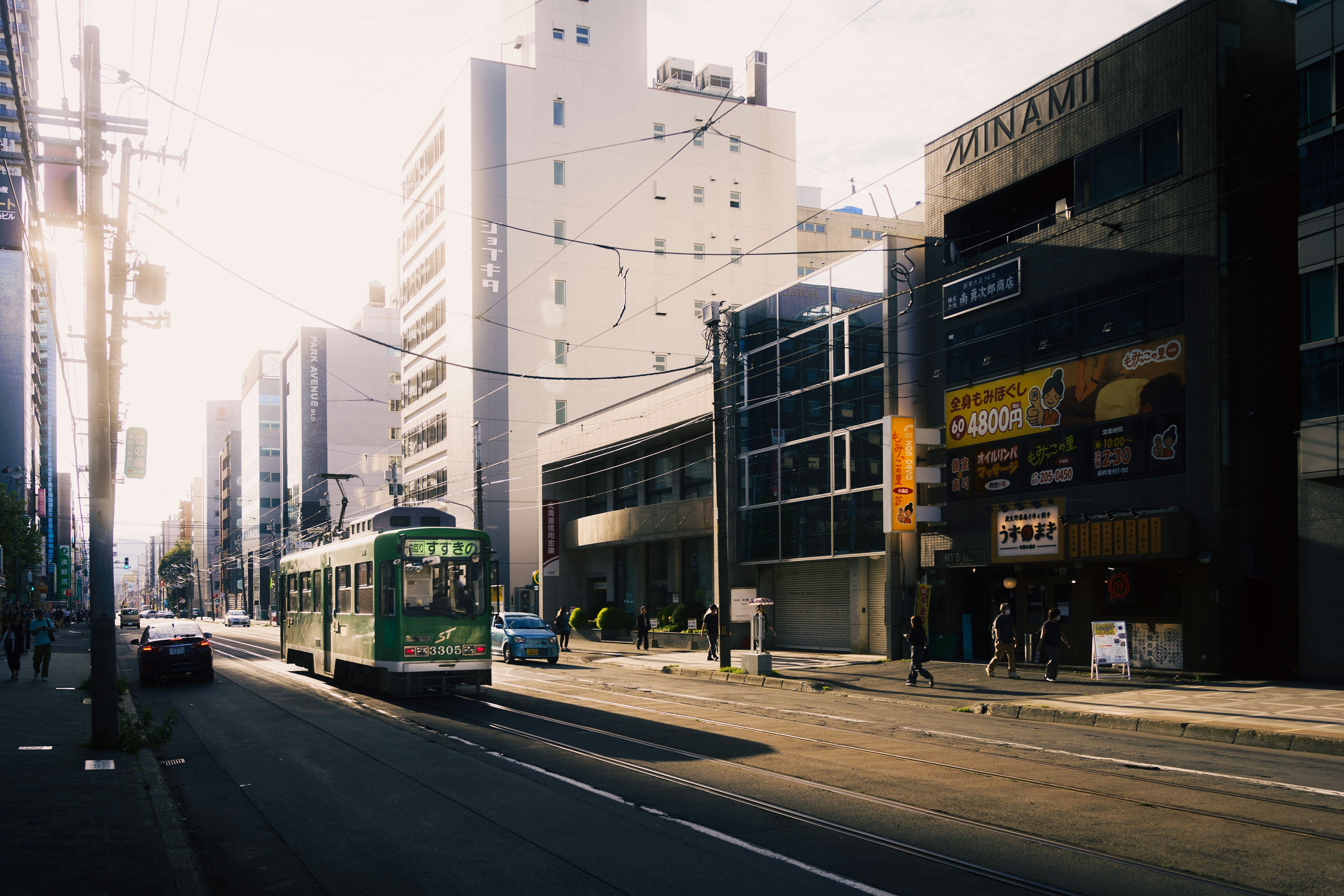 A green tram on an urban street with modern buildings