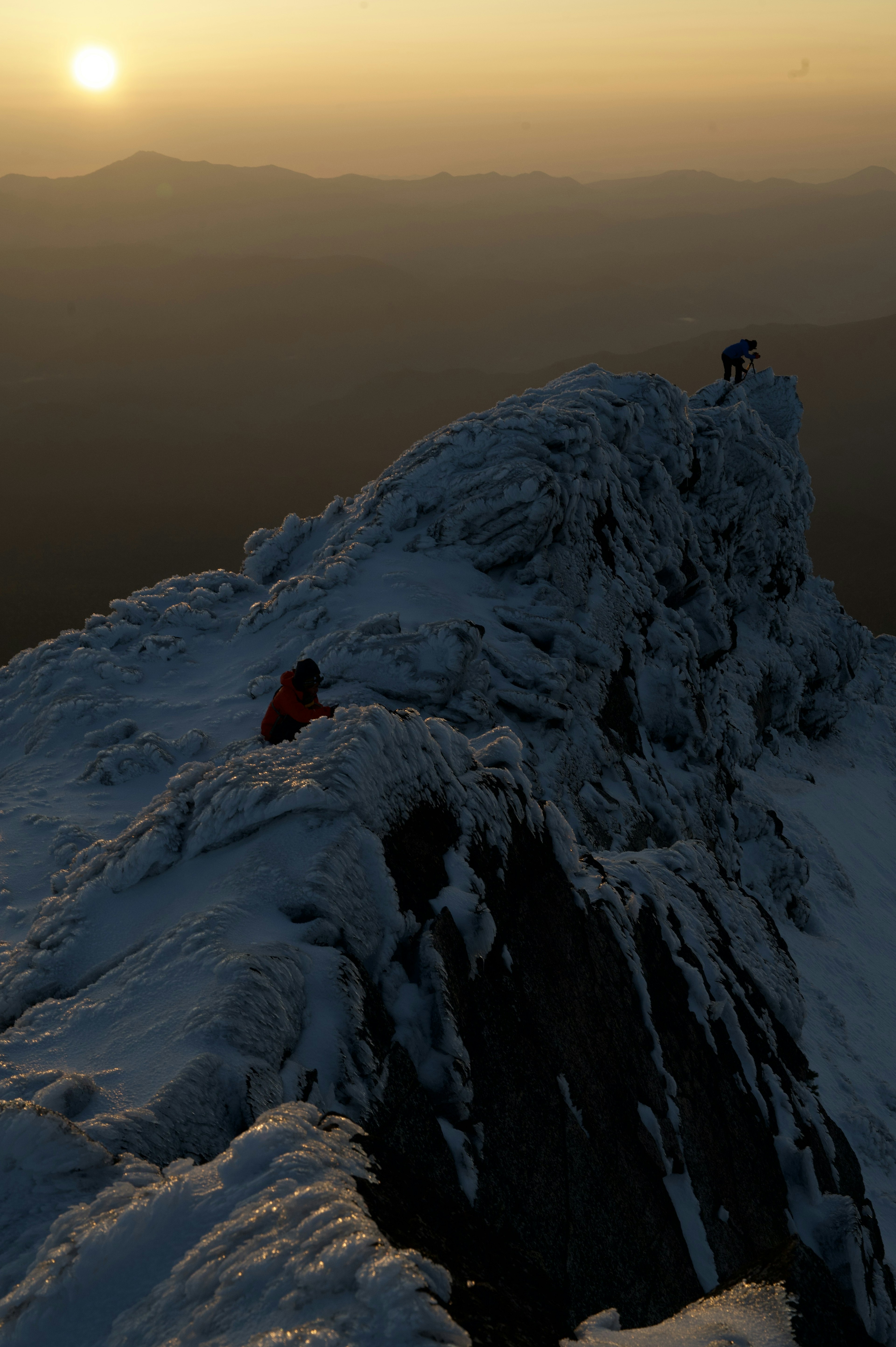 Escaladores navegando por una cresta nevada al atardecer en la cima de una montaña