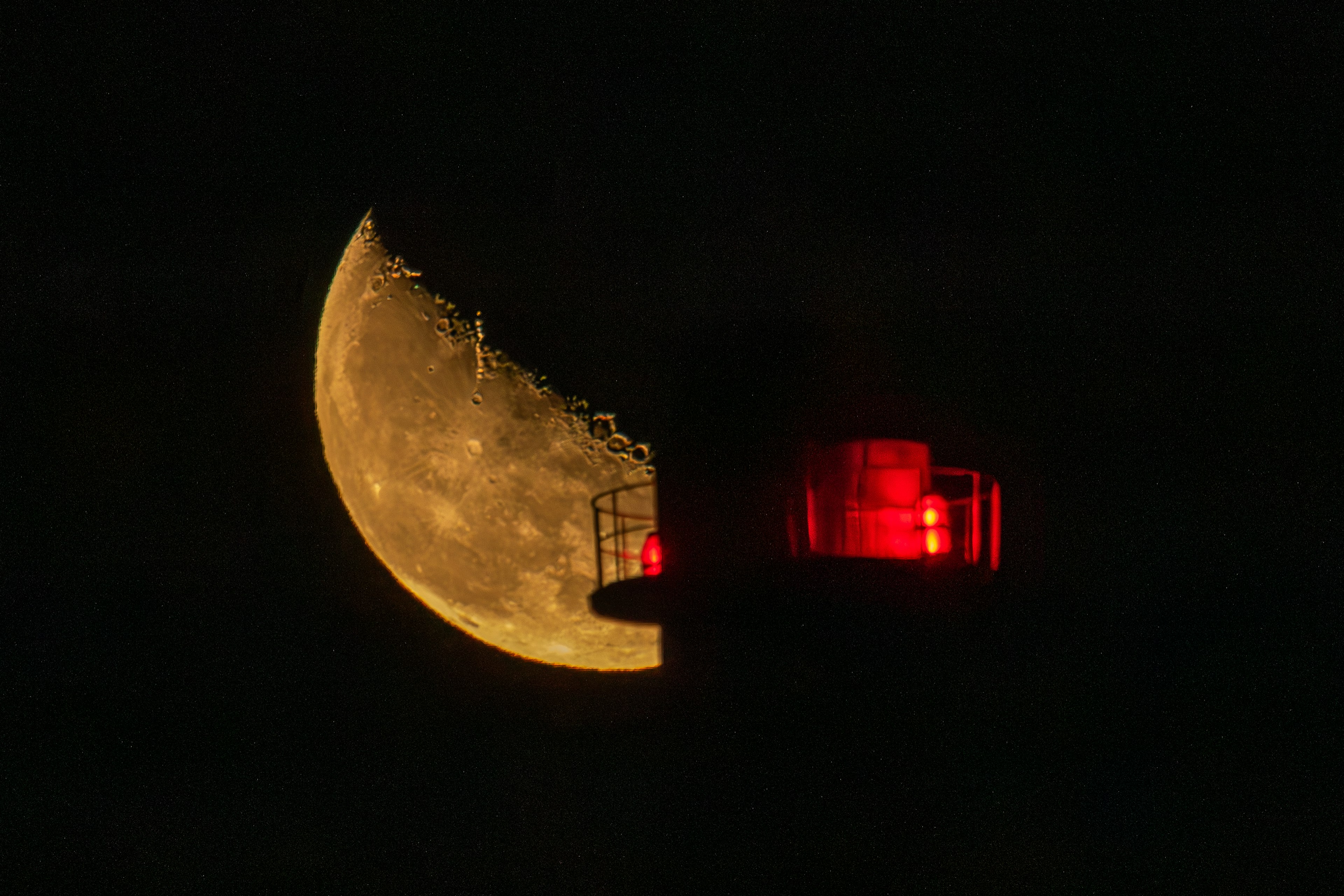 Half moon glowing in the night sky behind a red light