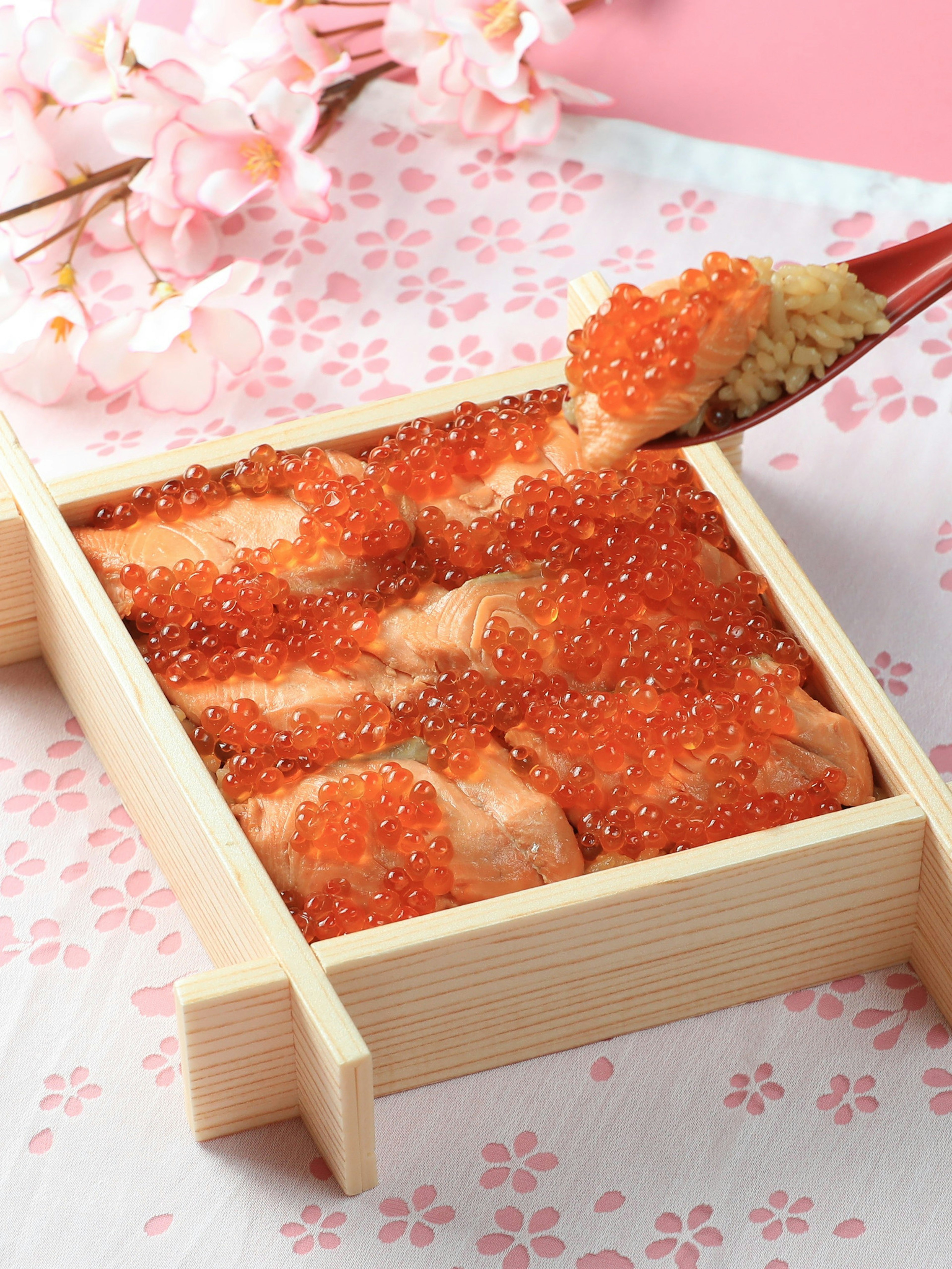 Wooden box filled with salmon sashimi and salmon roe on a pink floral background