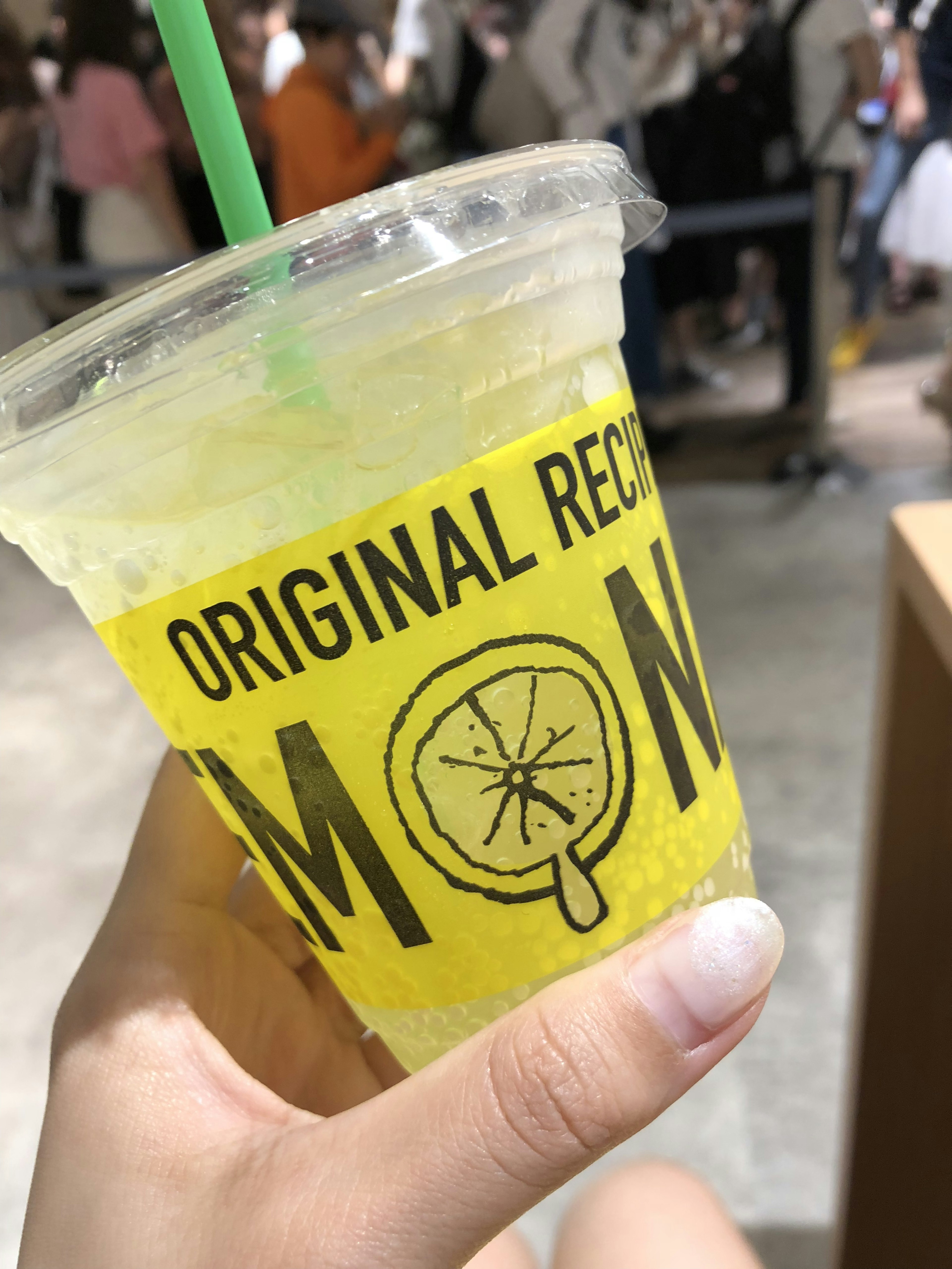 Tangan memegang gelas minuman lemon Label kuning dengan teks resep asli dan ilustrasi lemon