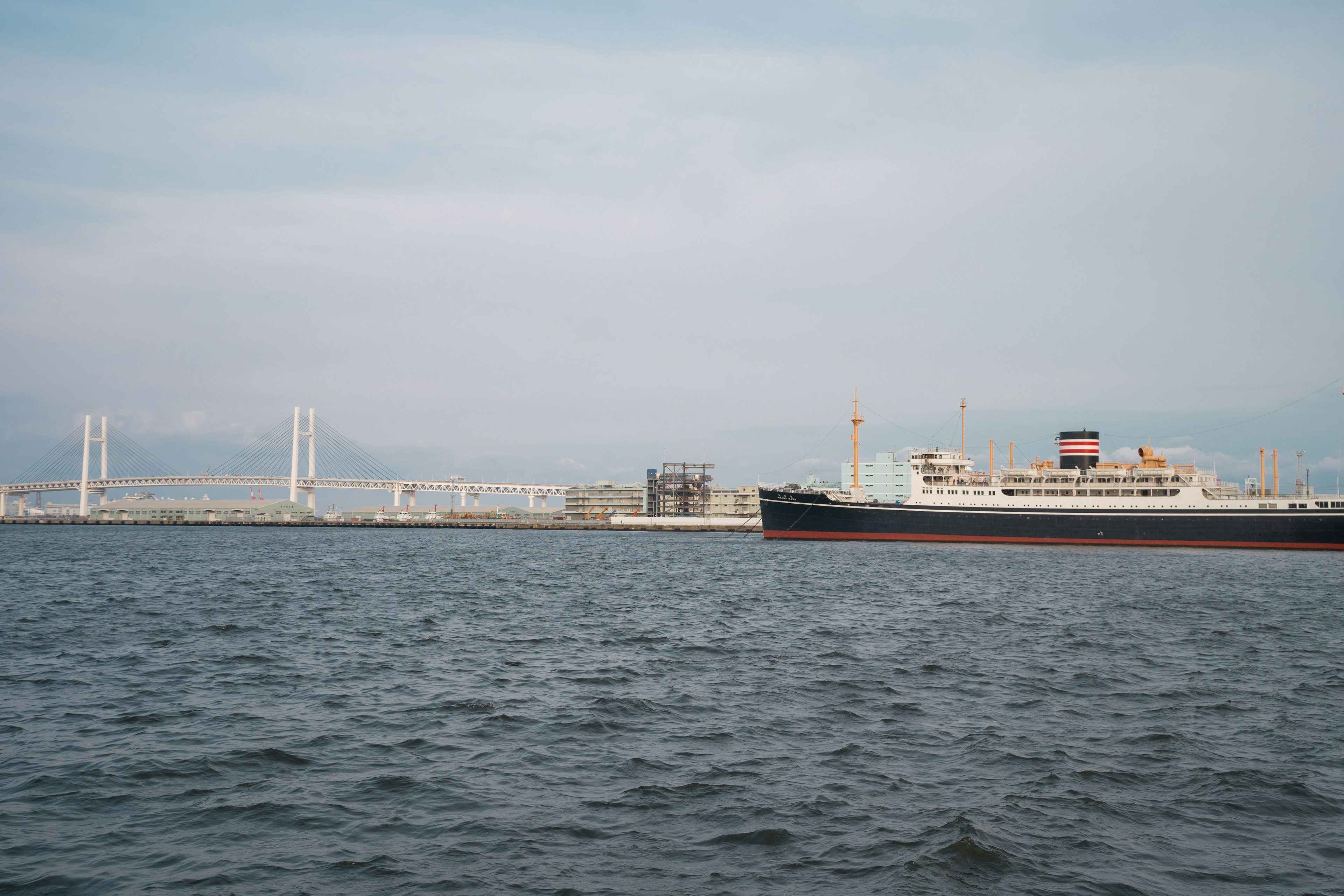 Large ship floating on the sea with a distant bridge visible