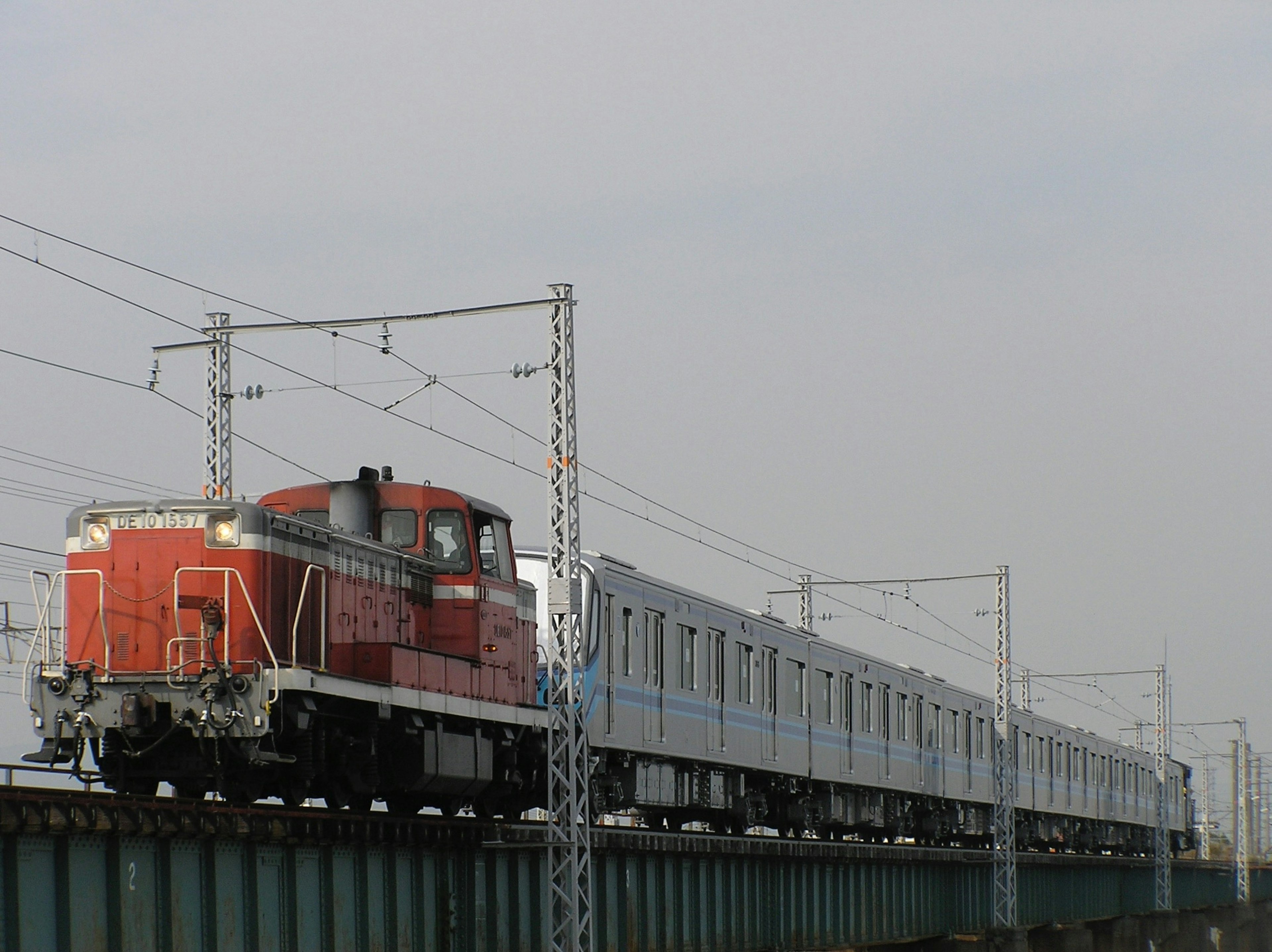 Locomotora roja tirando coches de pasajeros azules en un puente ferroviario