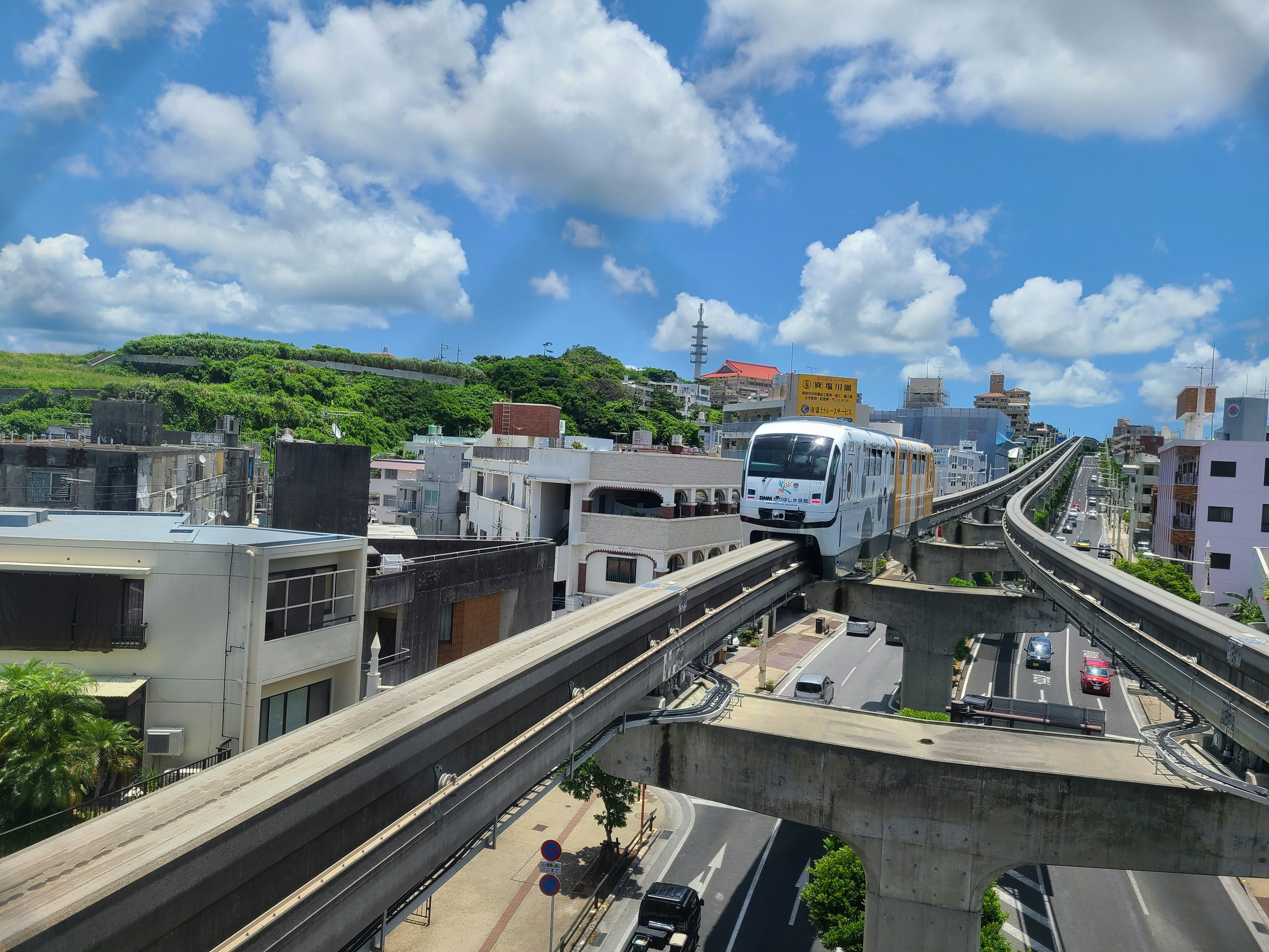 A monorail travels above a cityscape under a blue sky