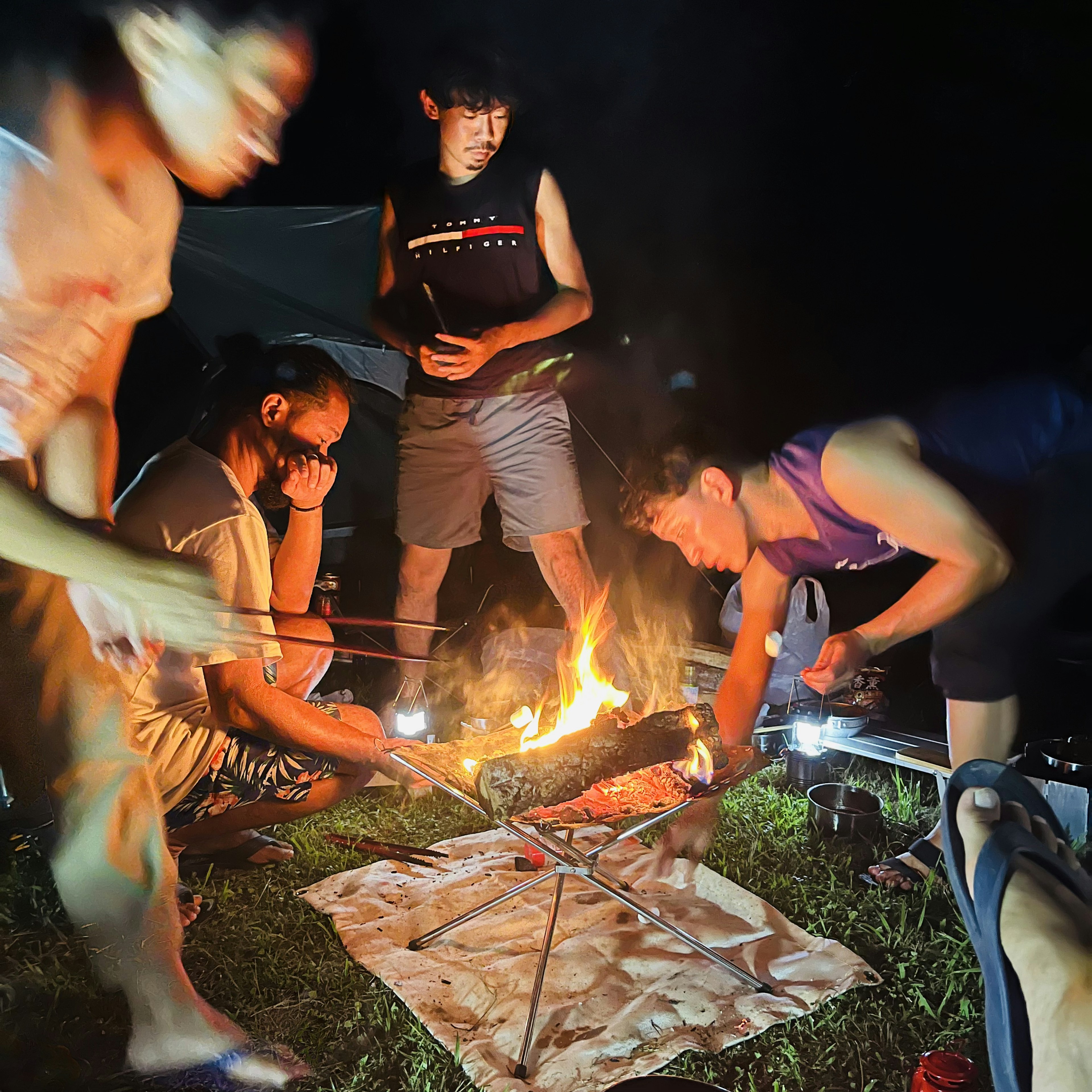 Persone riunite attorno a un fuoco durante un campeggio notturno mentre si godono un barbecue