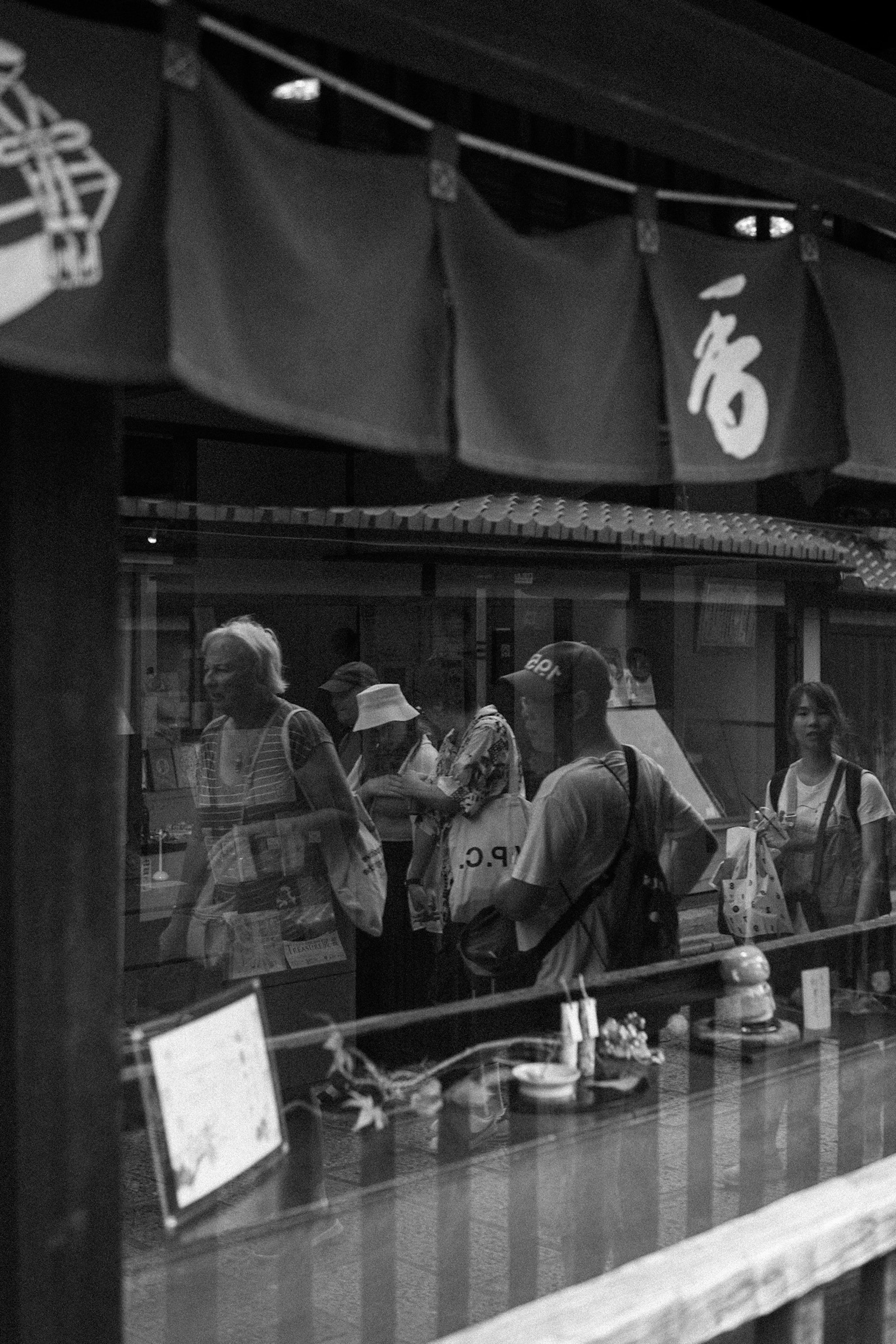 Black and white image of people queuing in front of a shop