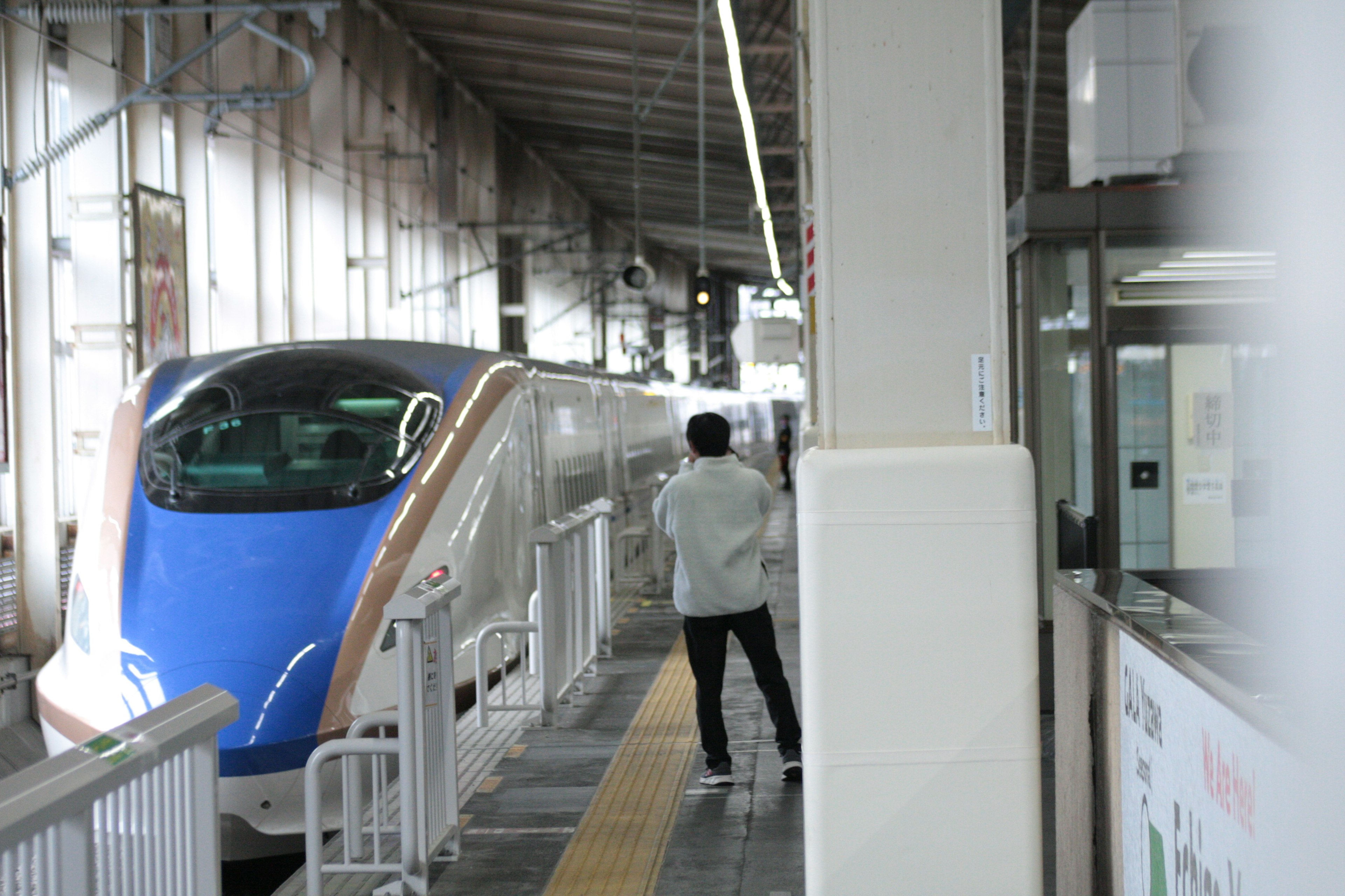 Seorang pria berdiri di platform stasiun dengan kereta biru yang diparkir