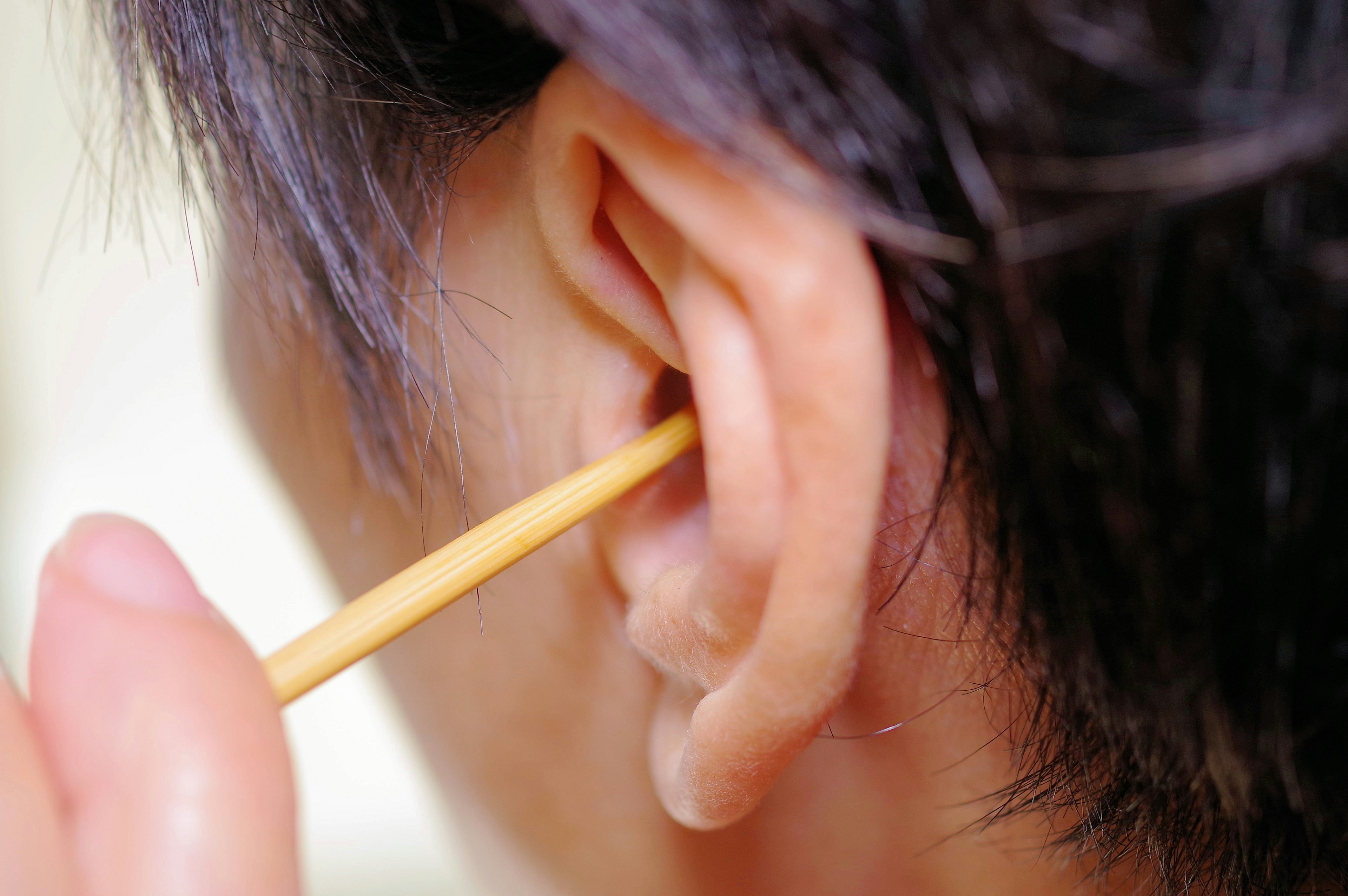 Close-up of a person cleaning their ear with a wooden stick