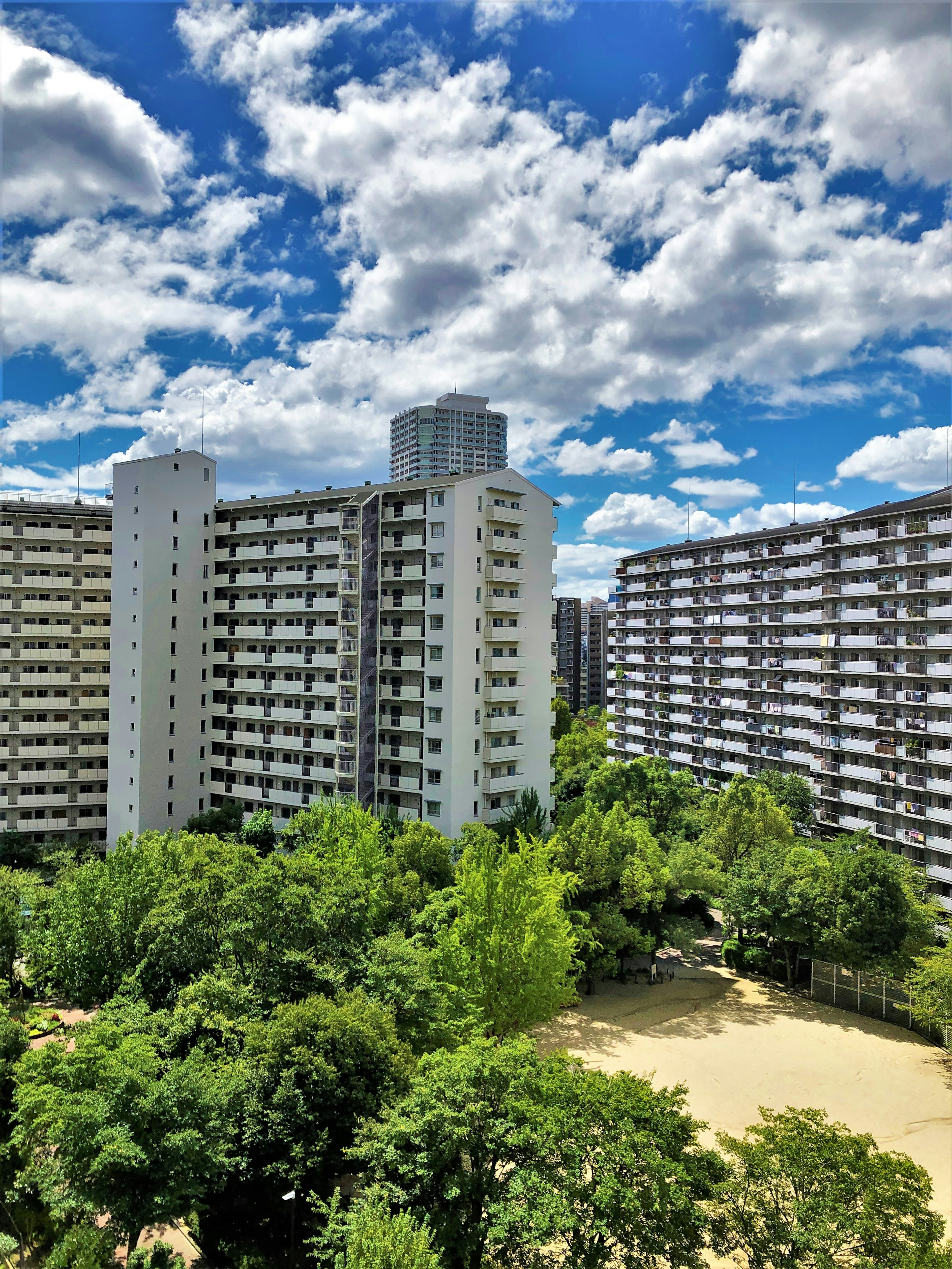 High-rise apartments under a blue sky with fluffy clouds and lush greenery