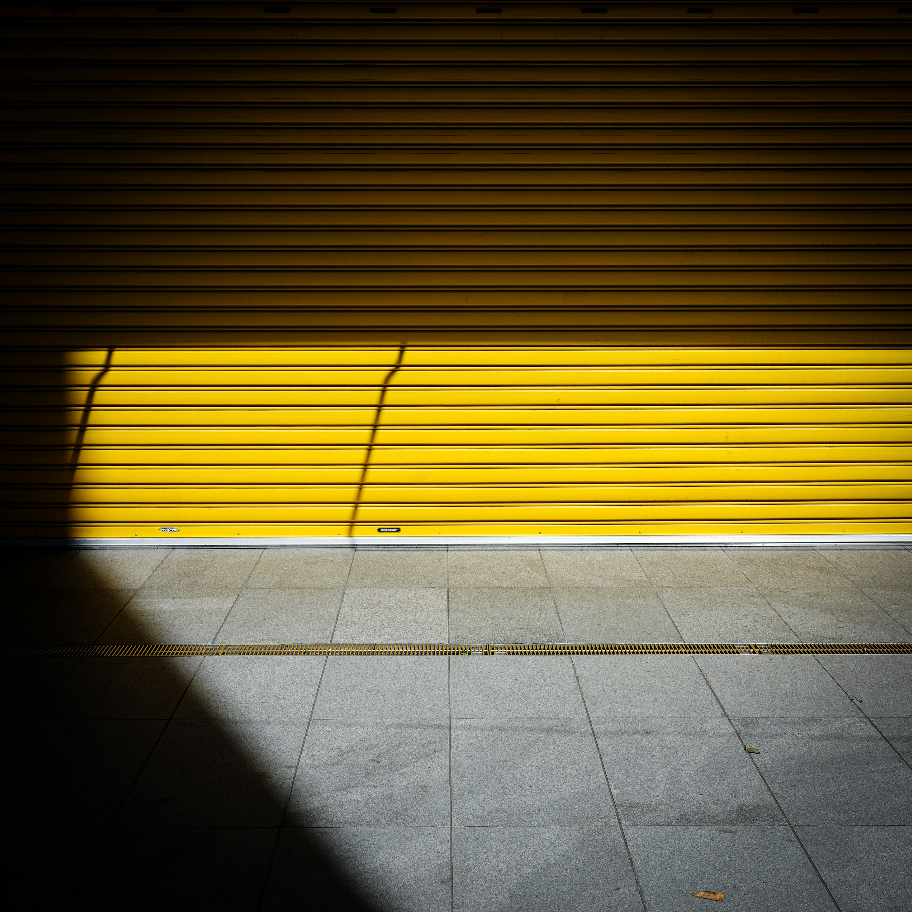 Kontrast zwischen einem gelben Rollladen und einem Schatten in einer städtischen Umgebung