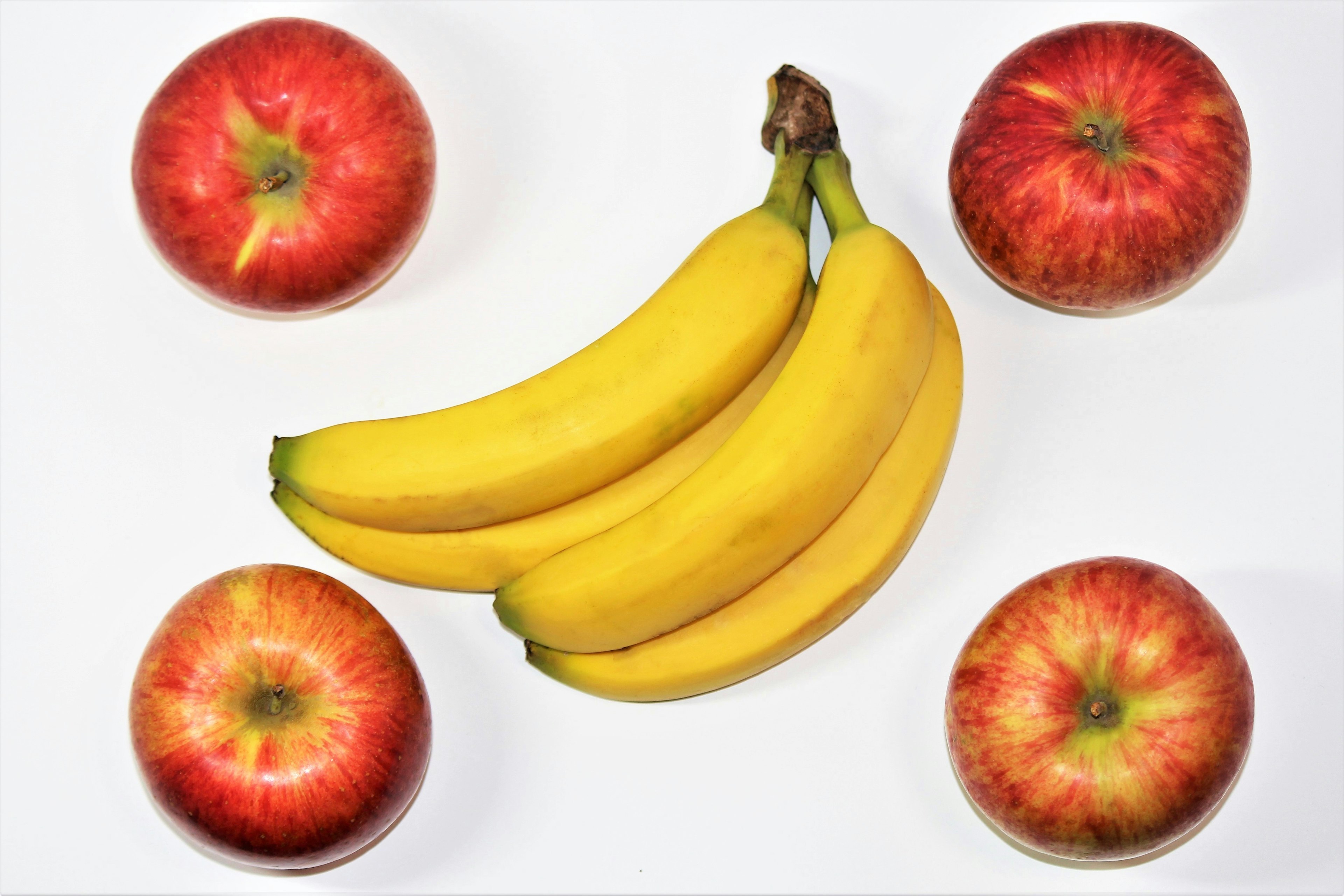 Mele rosse e banane gialle disposte su uno sfondo bianco