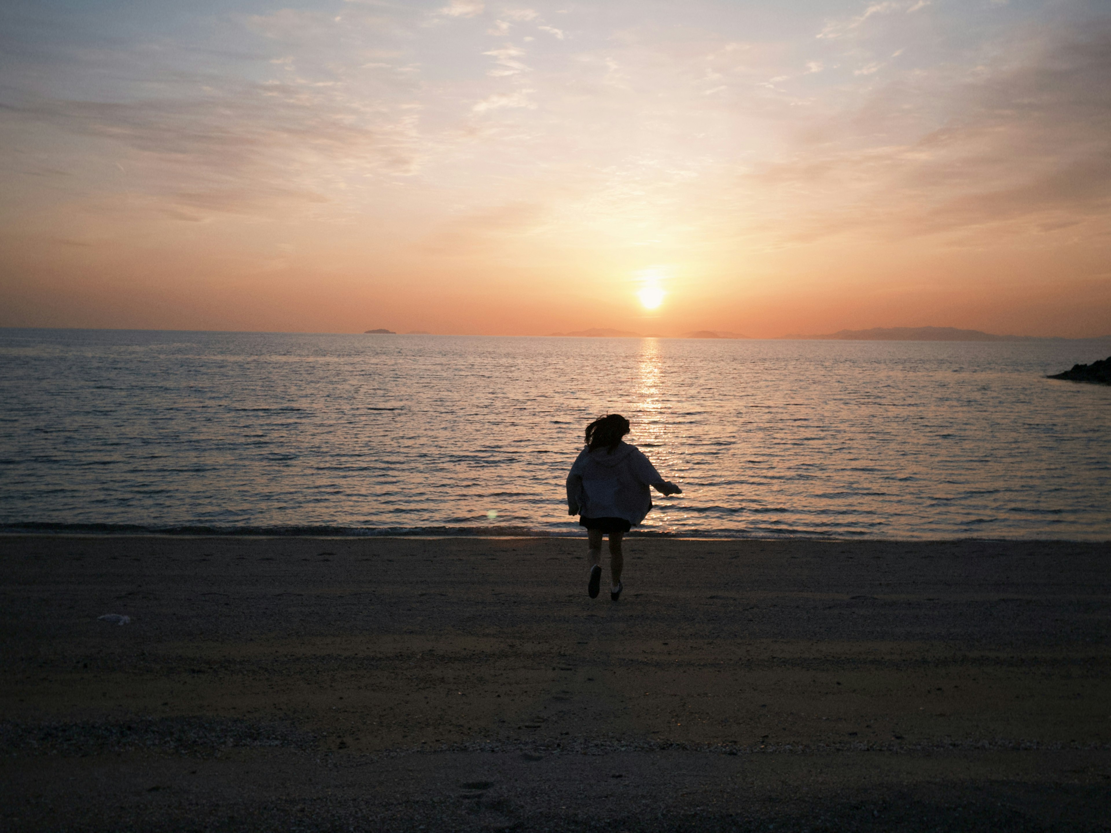 夕日を背にして海辺を走る女性のシルエット