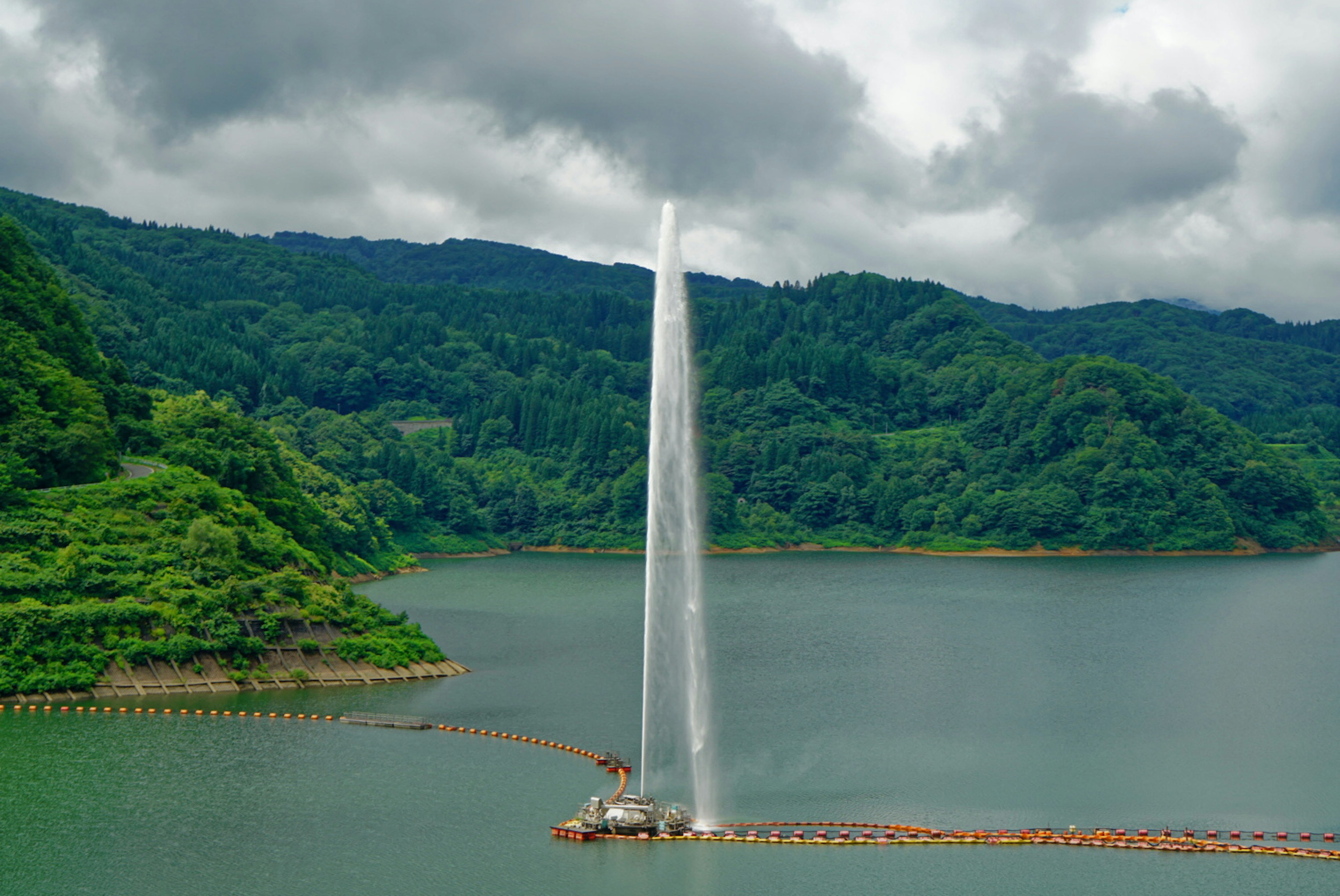 山々に囲まれた湖の中央に水が噴き上がる噴水