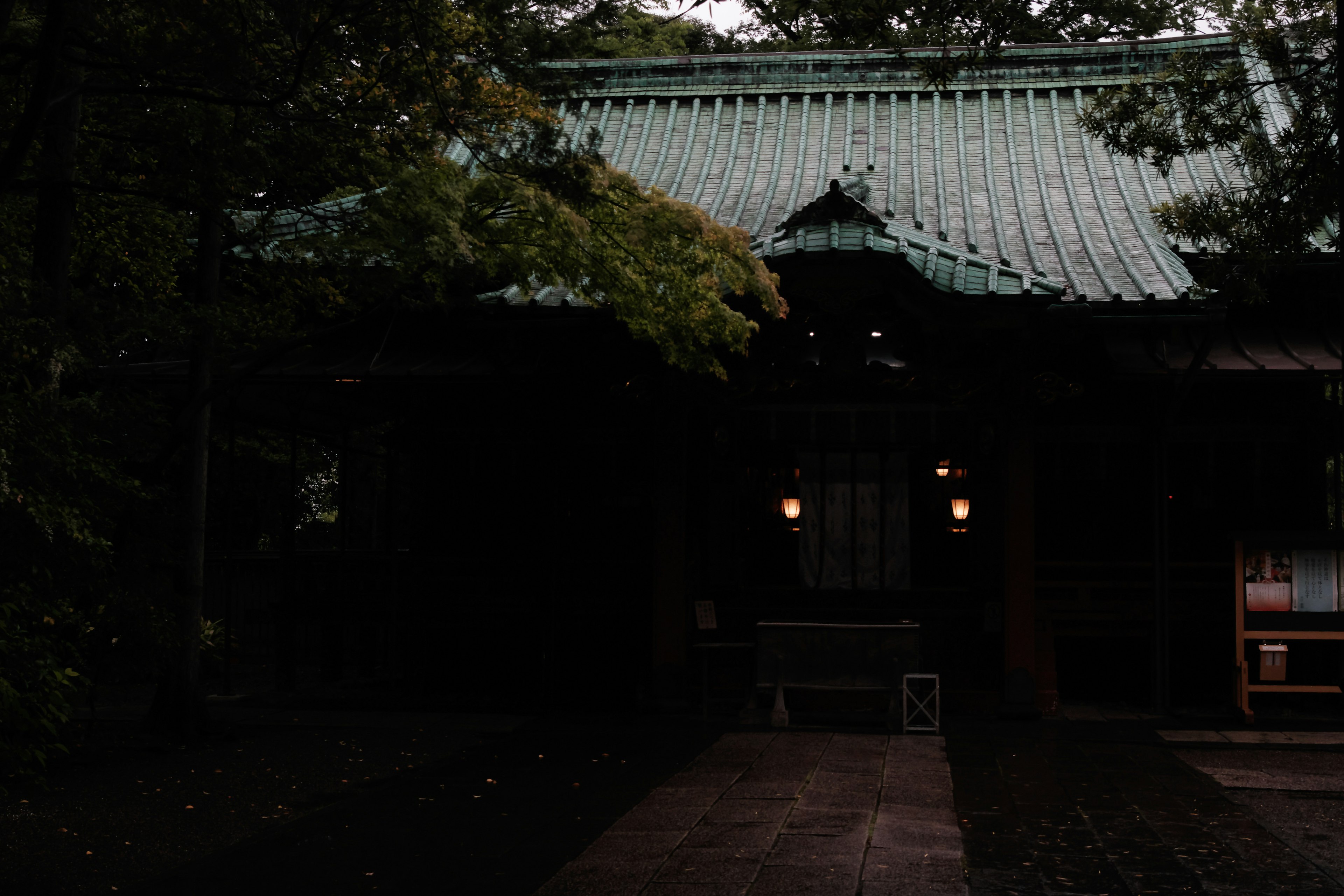 Exterior of a dark shrine with a green roof and surrounding trees