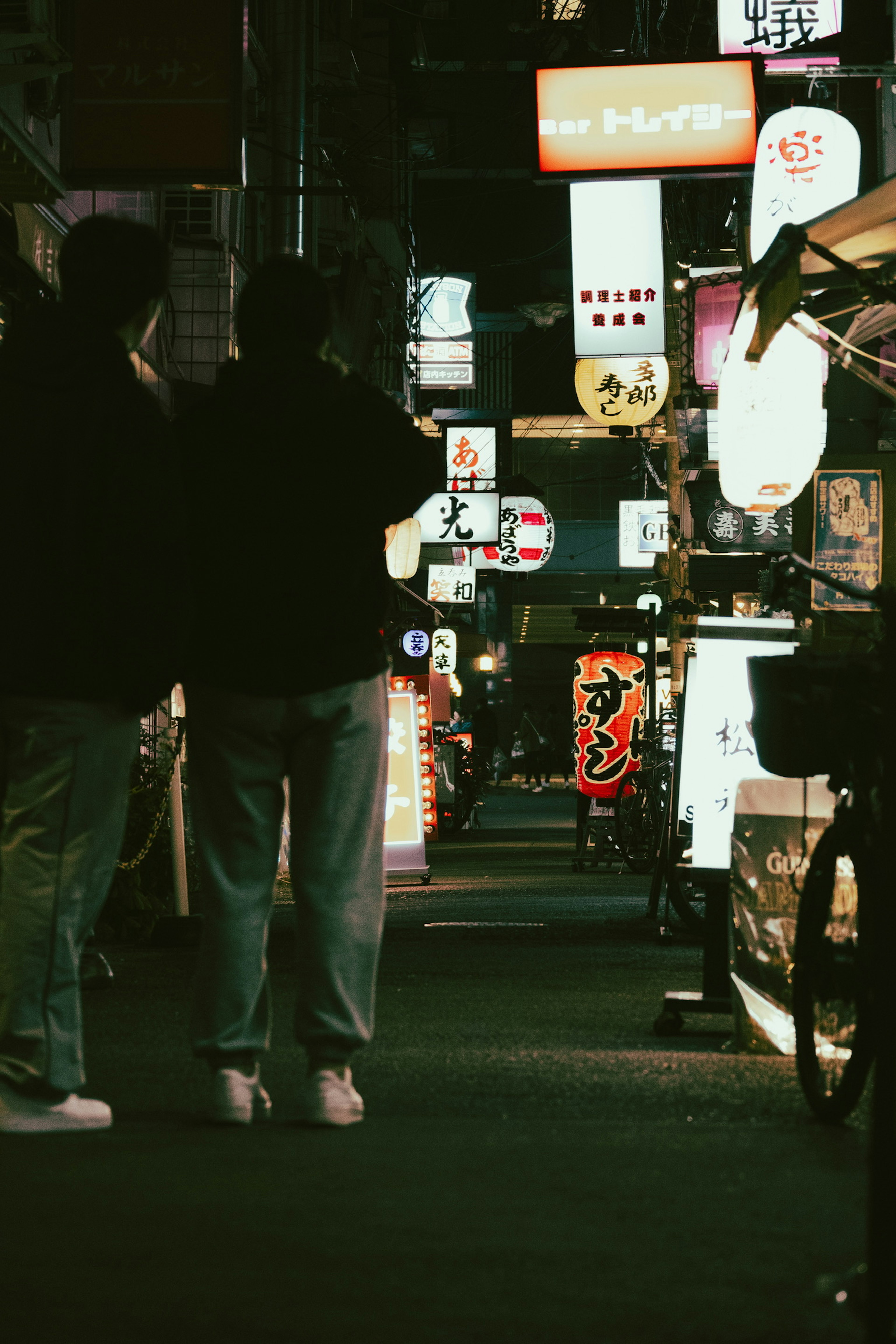 Two people standing in a dark street with bright lanterns lining the path