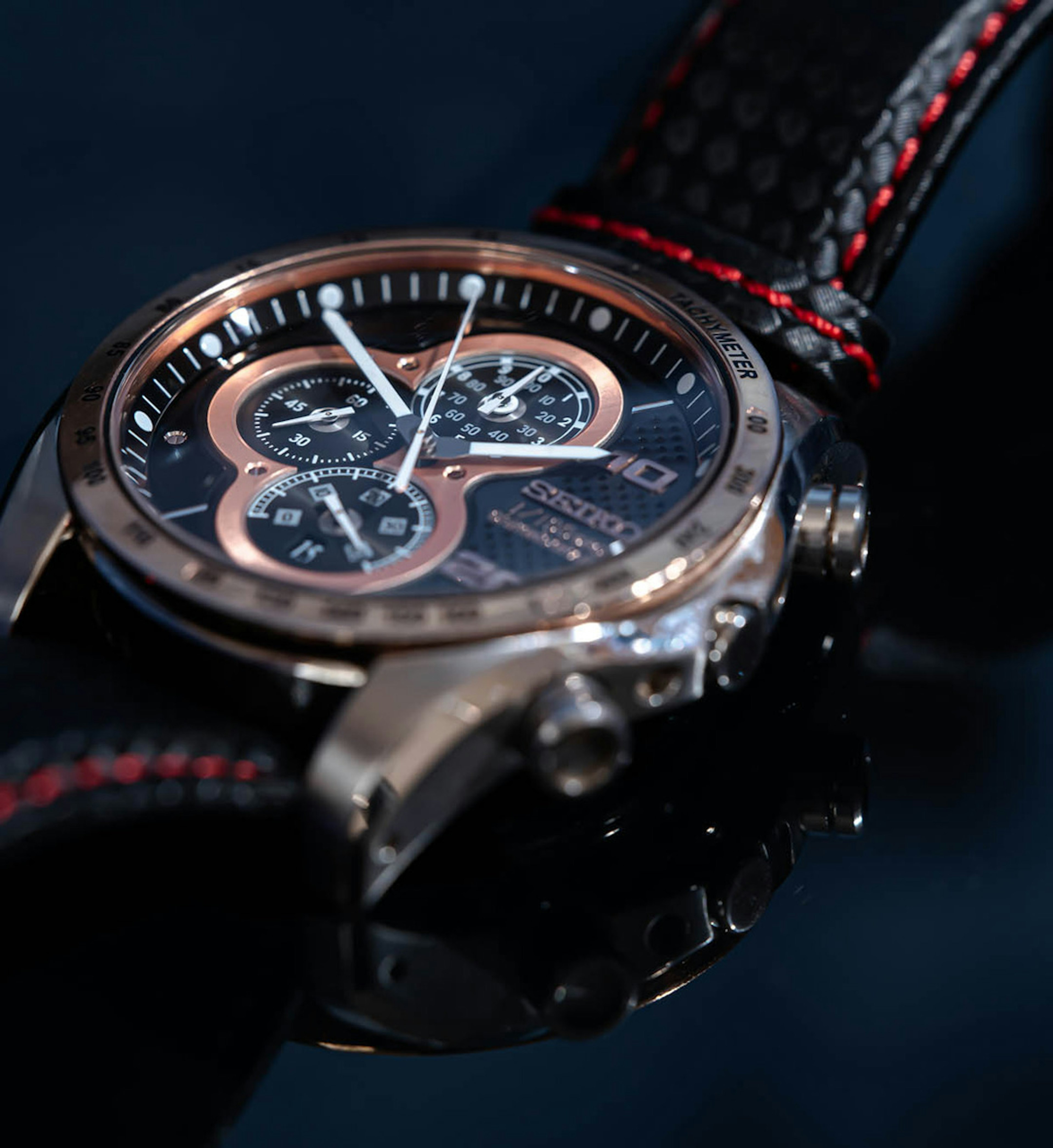 Close-up of a luxury watch reflecting on a black background featuring copper accents and a dark dial