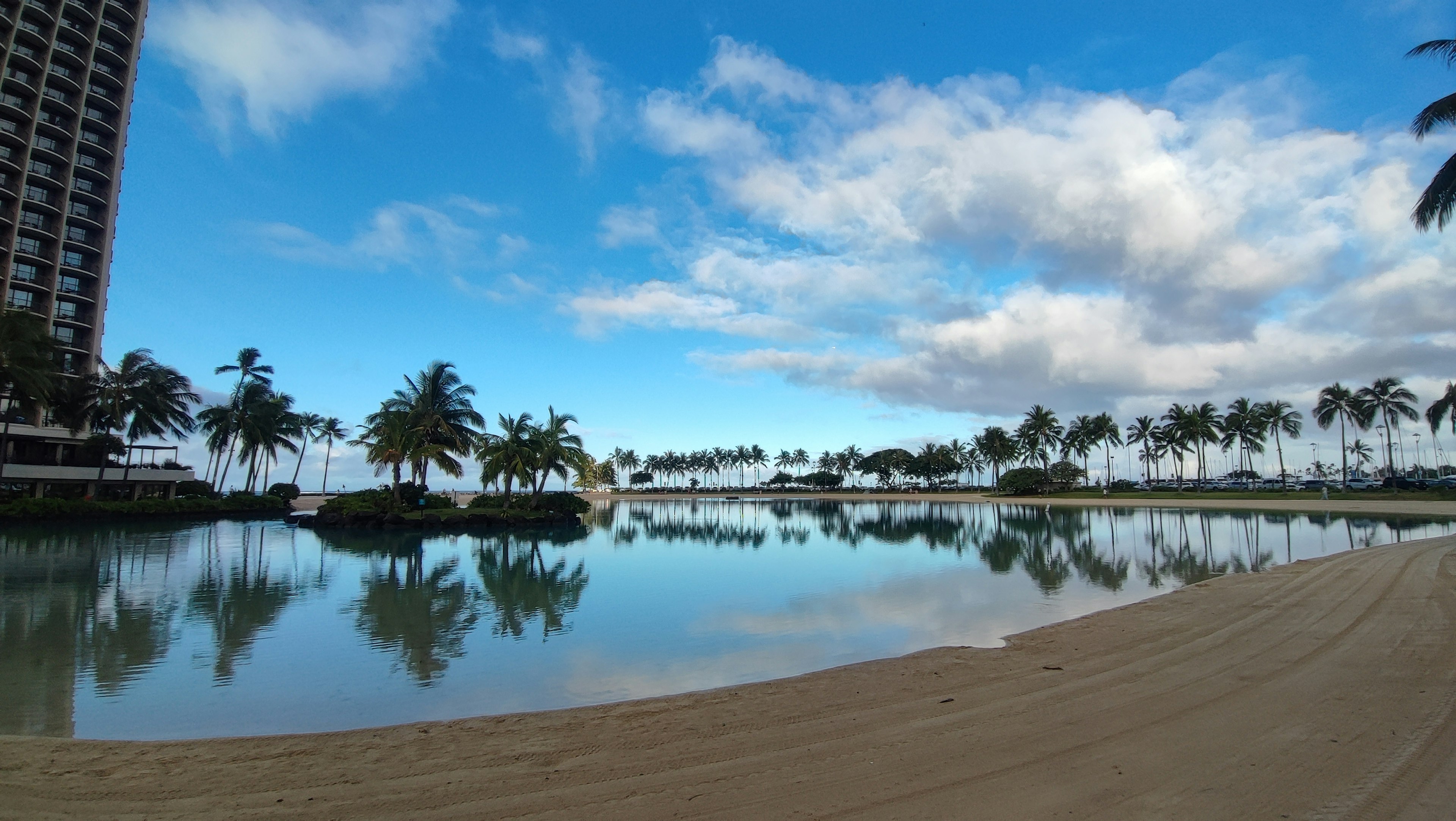 Lagoon ที่สวยงามสะท้อนท้องฟ้าสีฟ้าและเมฆ พร้อมต้นปาล์มและชายหาดทราย