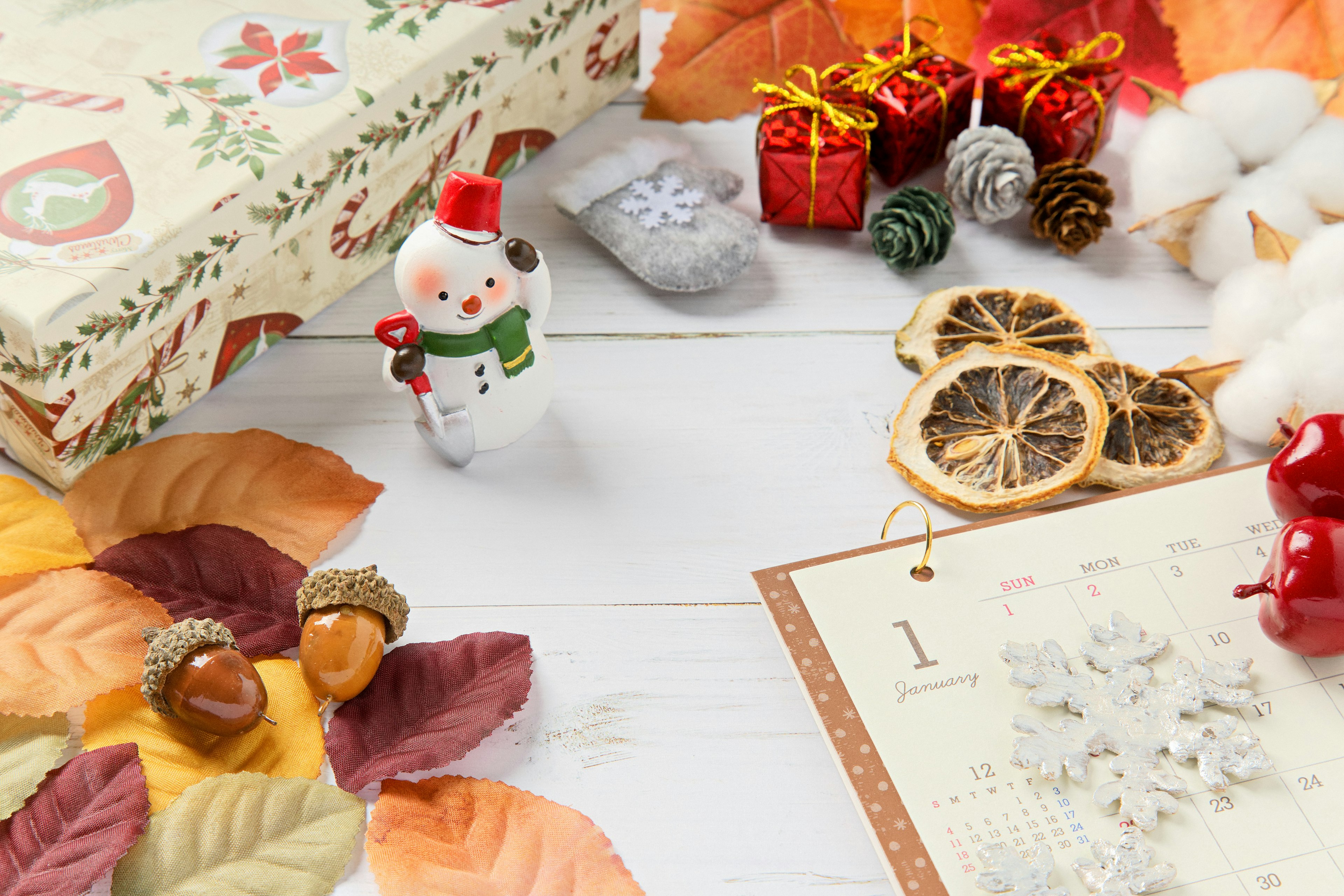 Small snowman figurine surrounded by Christmas decorations and autumn leaves