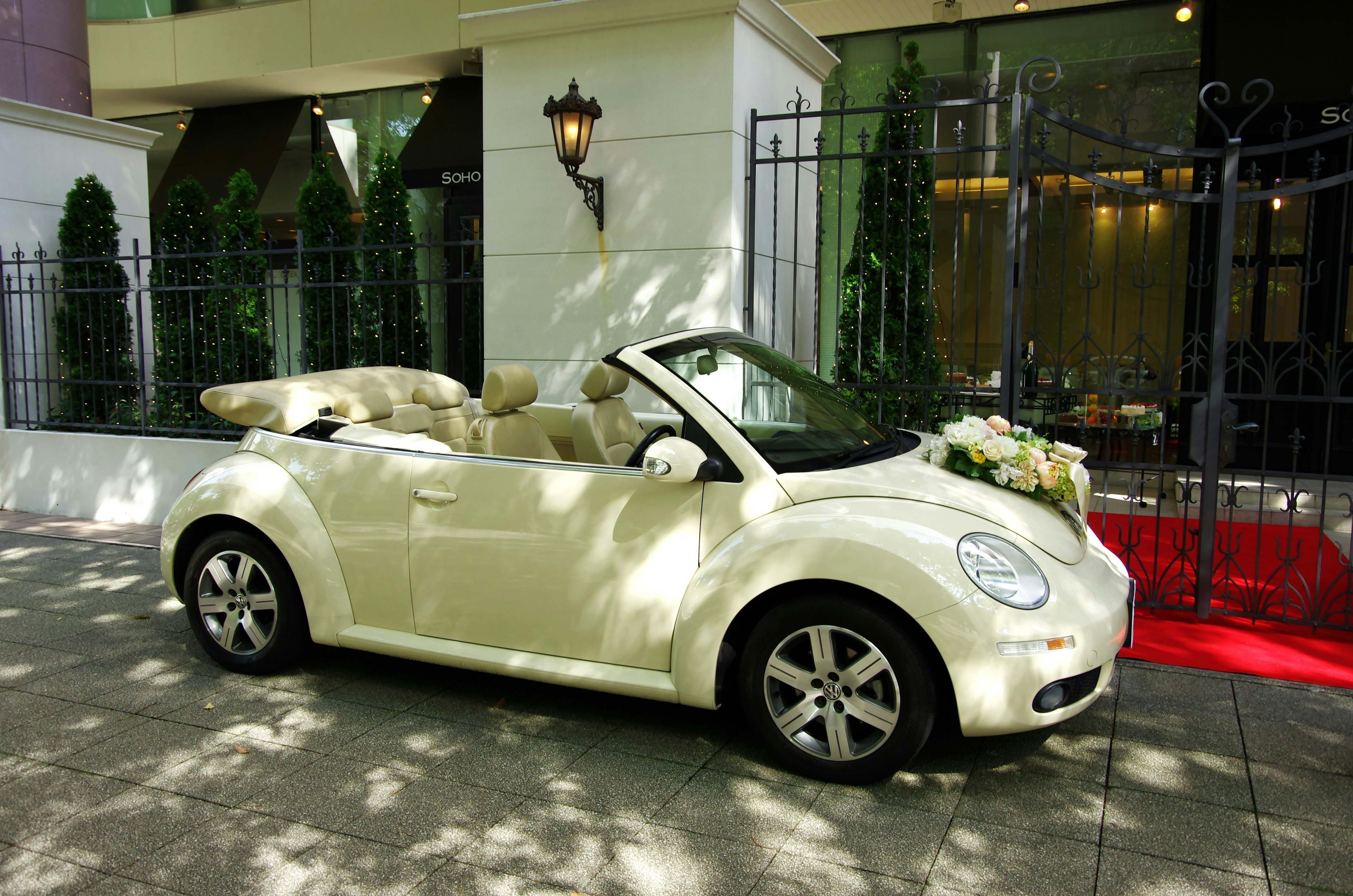 Un coche convertible Beetle blanco decorado con flores estacionado frente a un edificio elegante