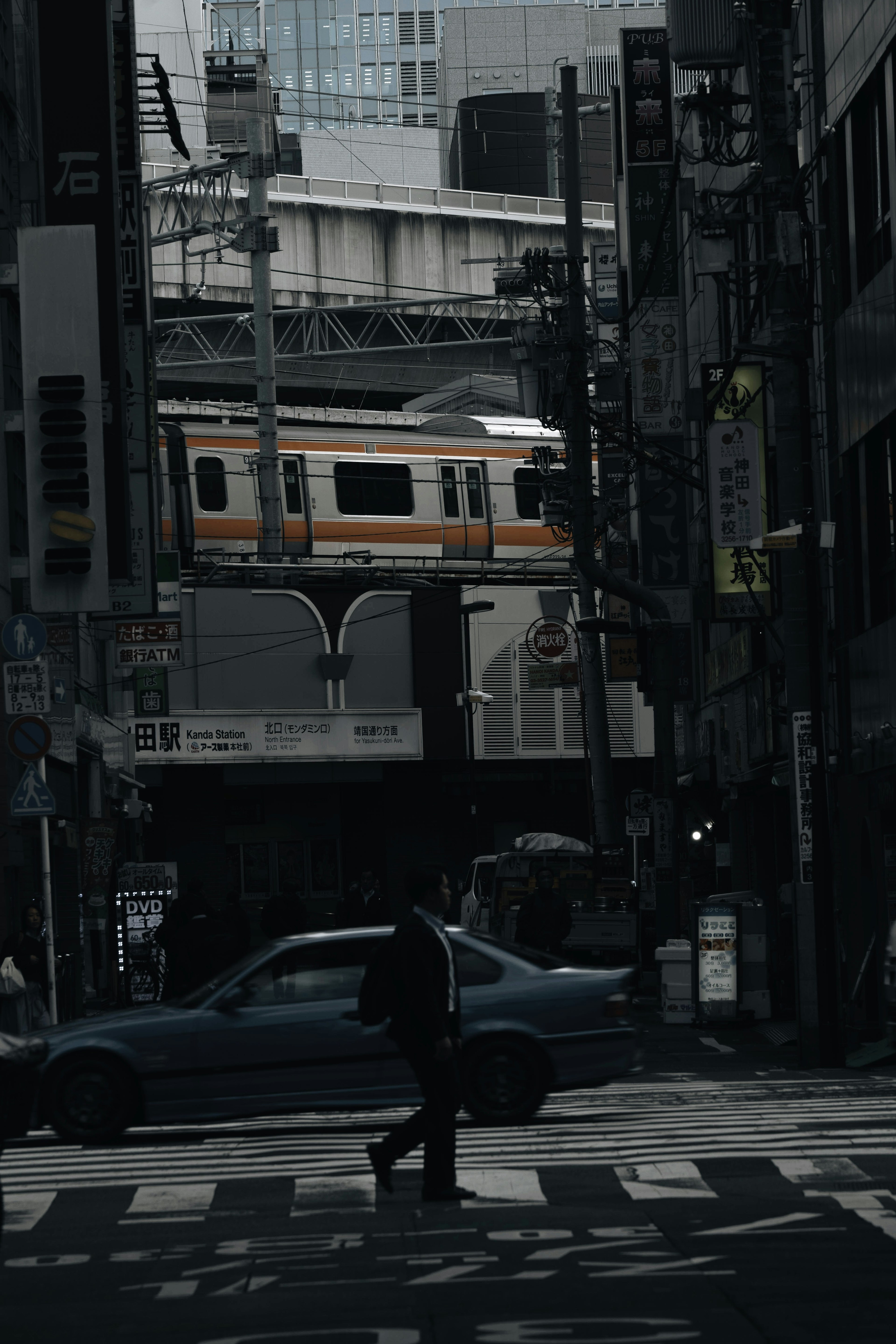 A person crossing the street in a dark urban setting with an elevated train