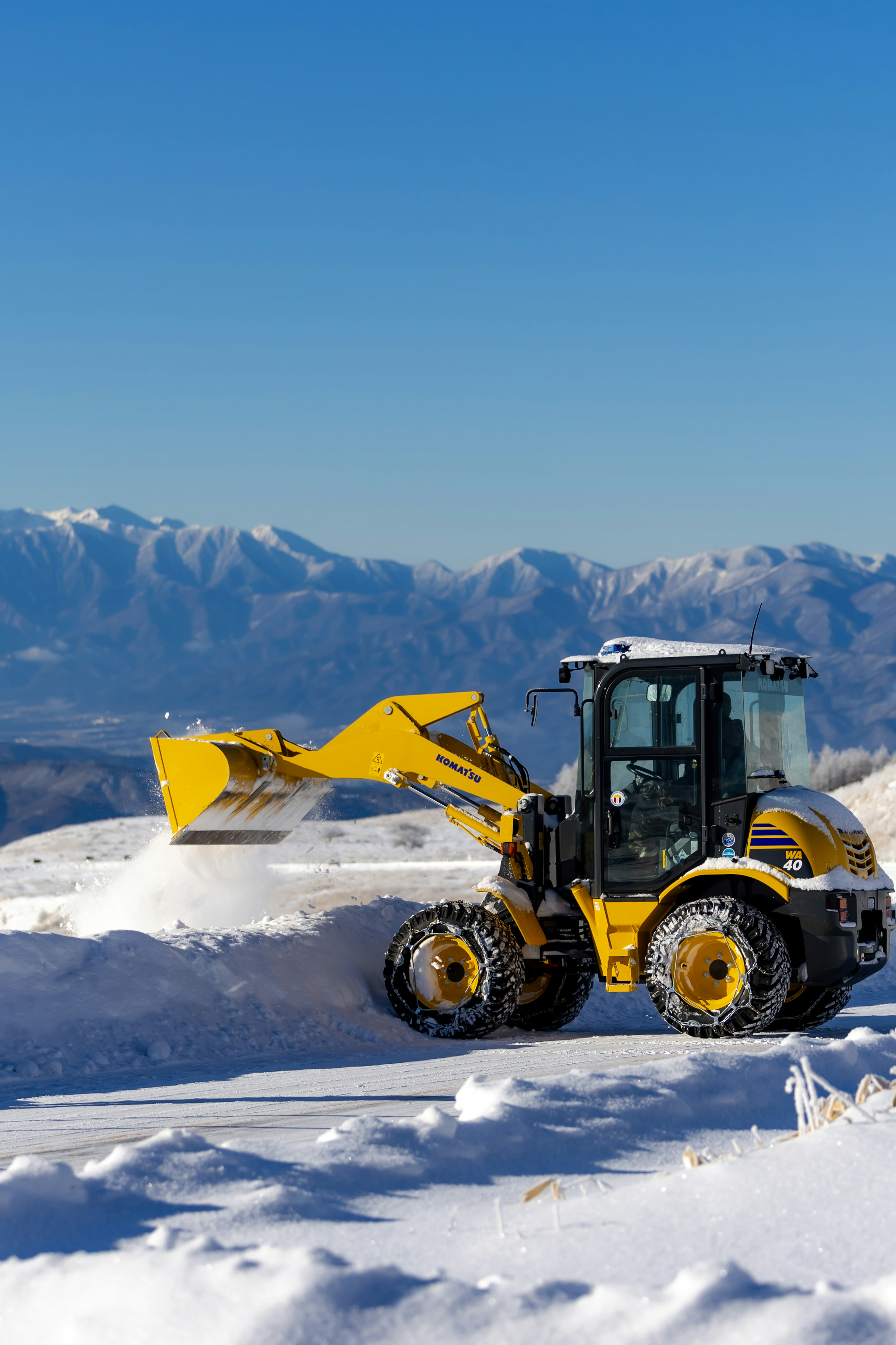 Bétonnière jaune travaillant dans la neige avec un arrière-plan de montagnes