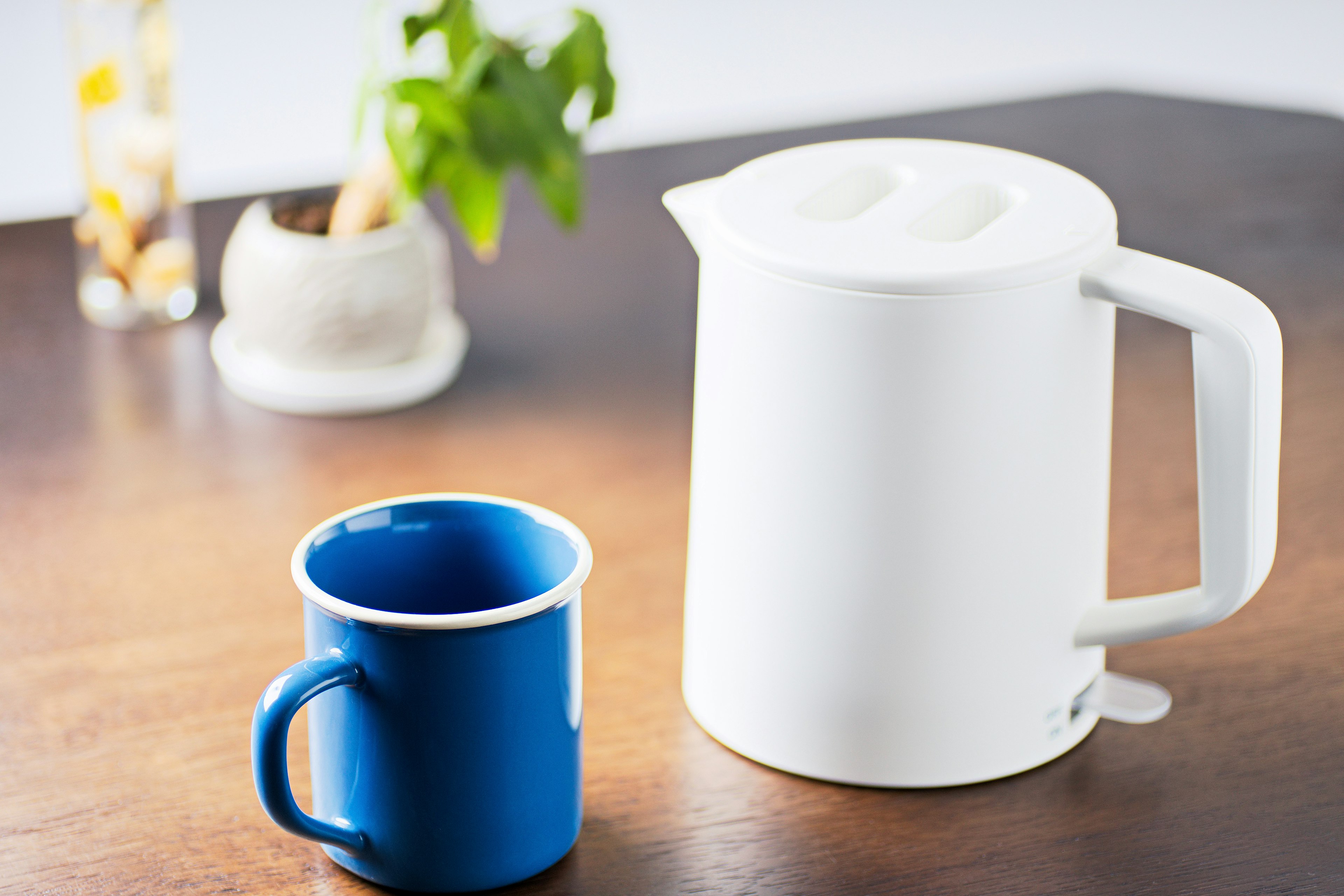 Une bouilloire électrique blanche et une tasse bleue posées sur une table en bois