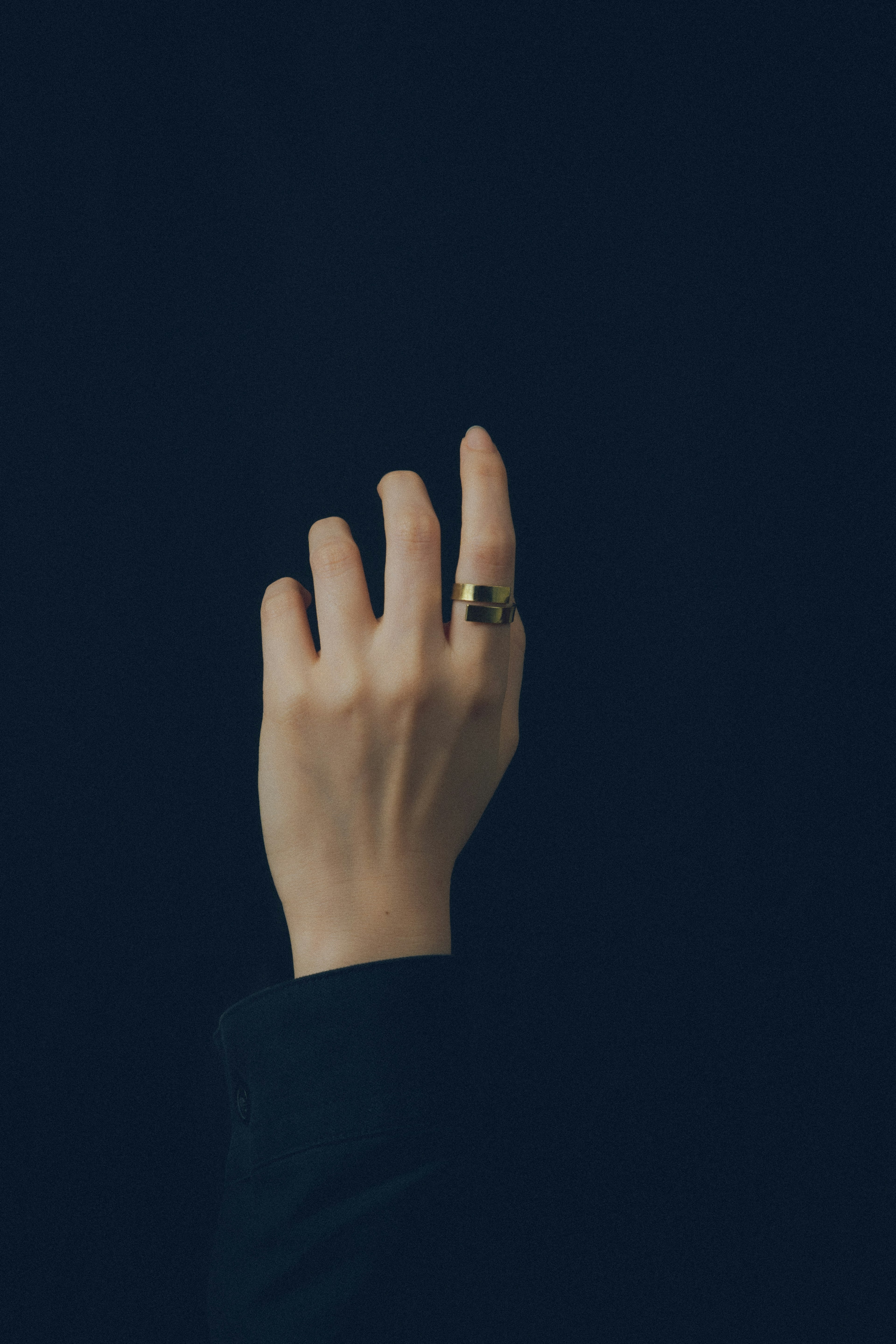 A hand raised against a dark background featuring a ring on the finger