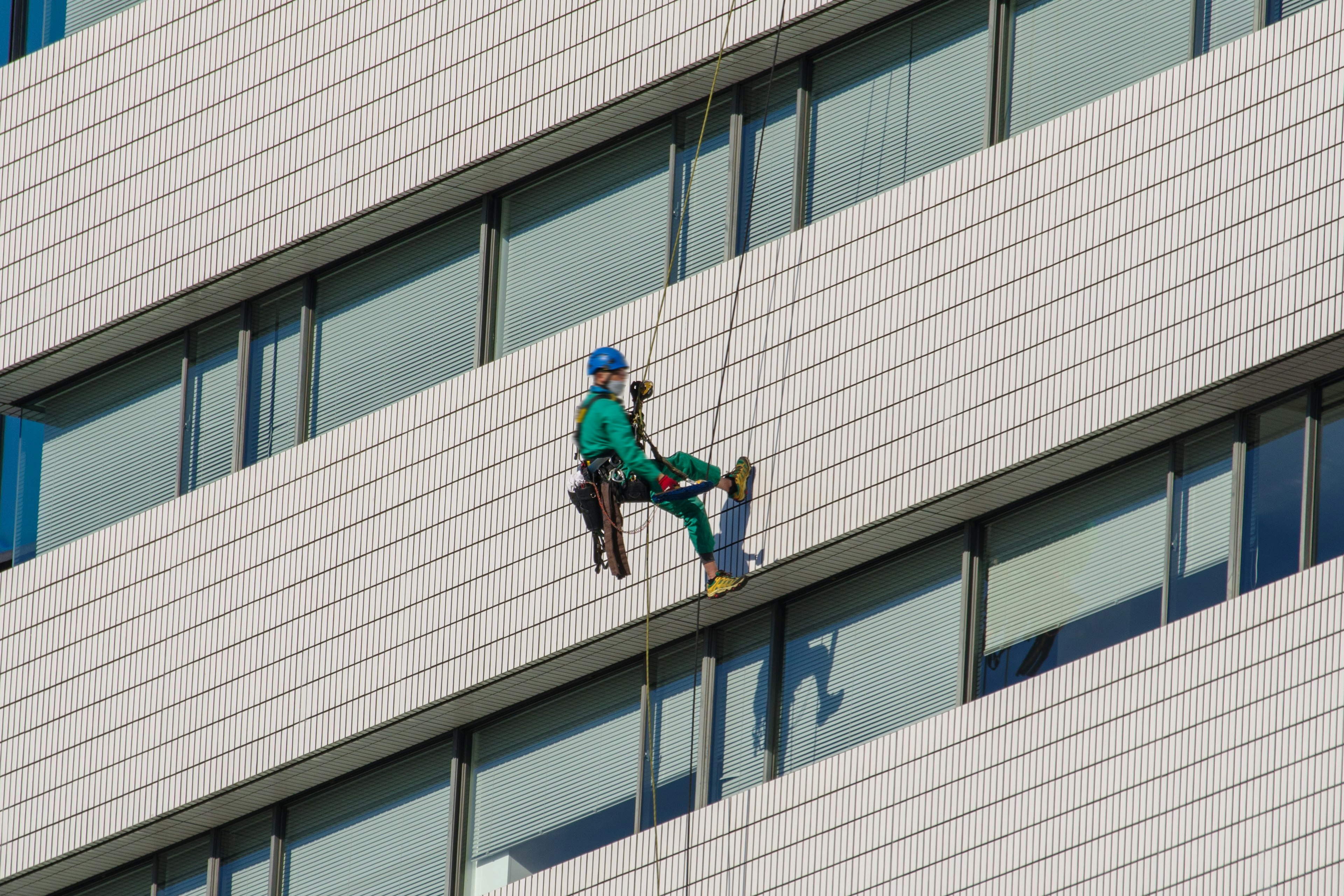 Worker in green uniform cleaning the exterior of a high-rise building