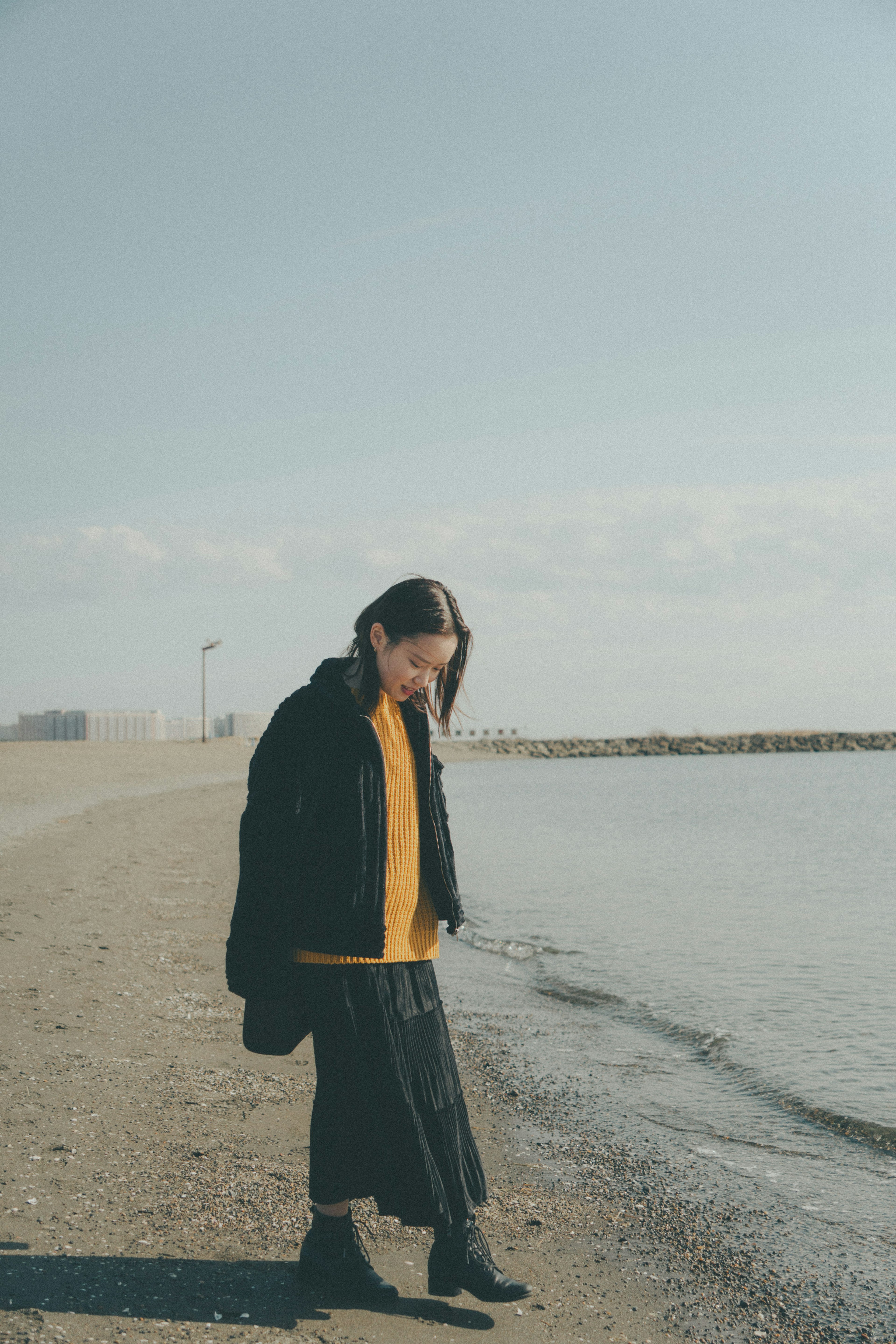 Femme marchant sur la plage portant un manteau noir et un haut jaune