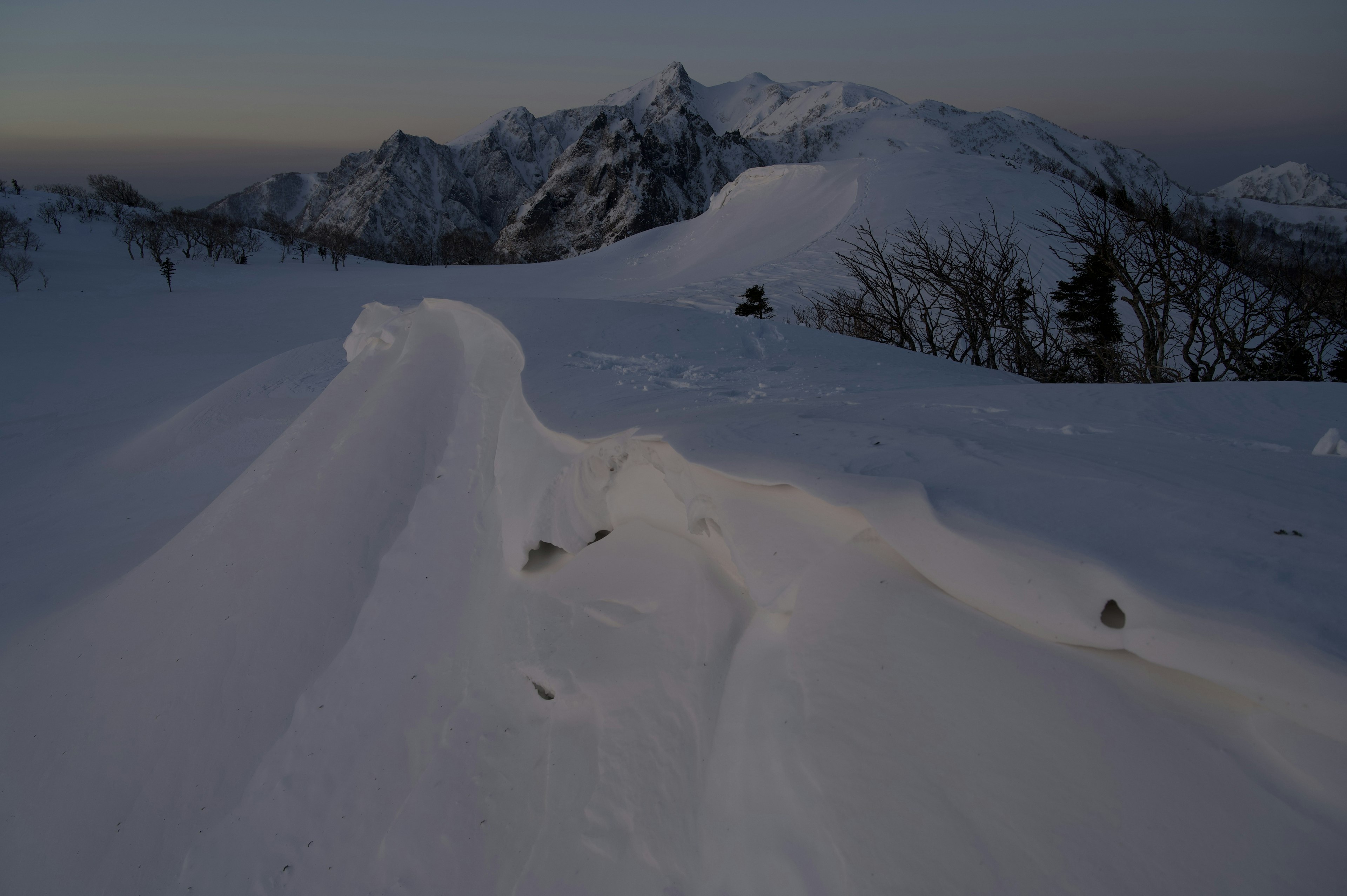 Schneebedeckte Berglandschaft mit gewellten Schneeflächen in der Dämmerung