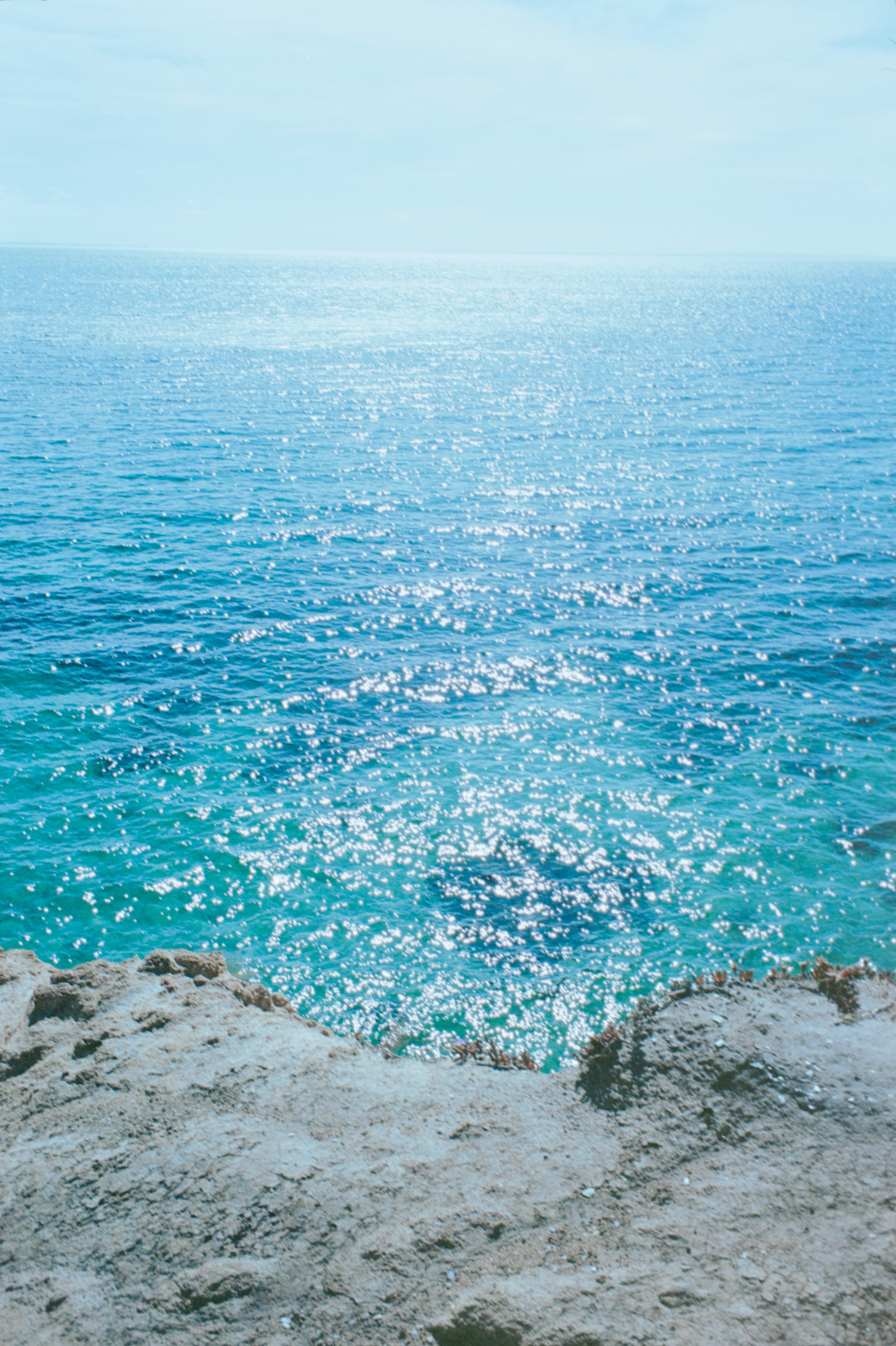 Vista da una scogliera su un oceano blu scintillante con riflessi di luce