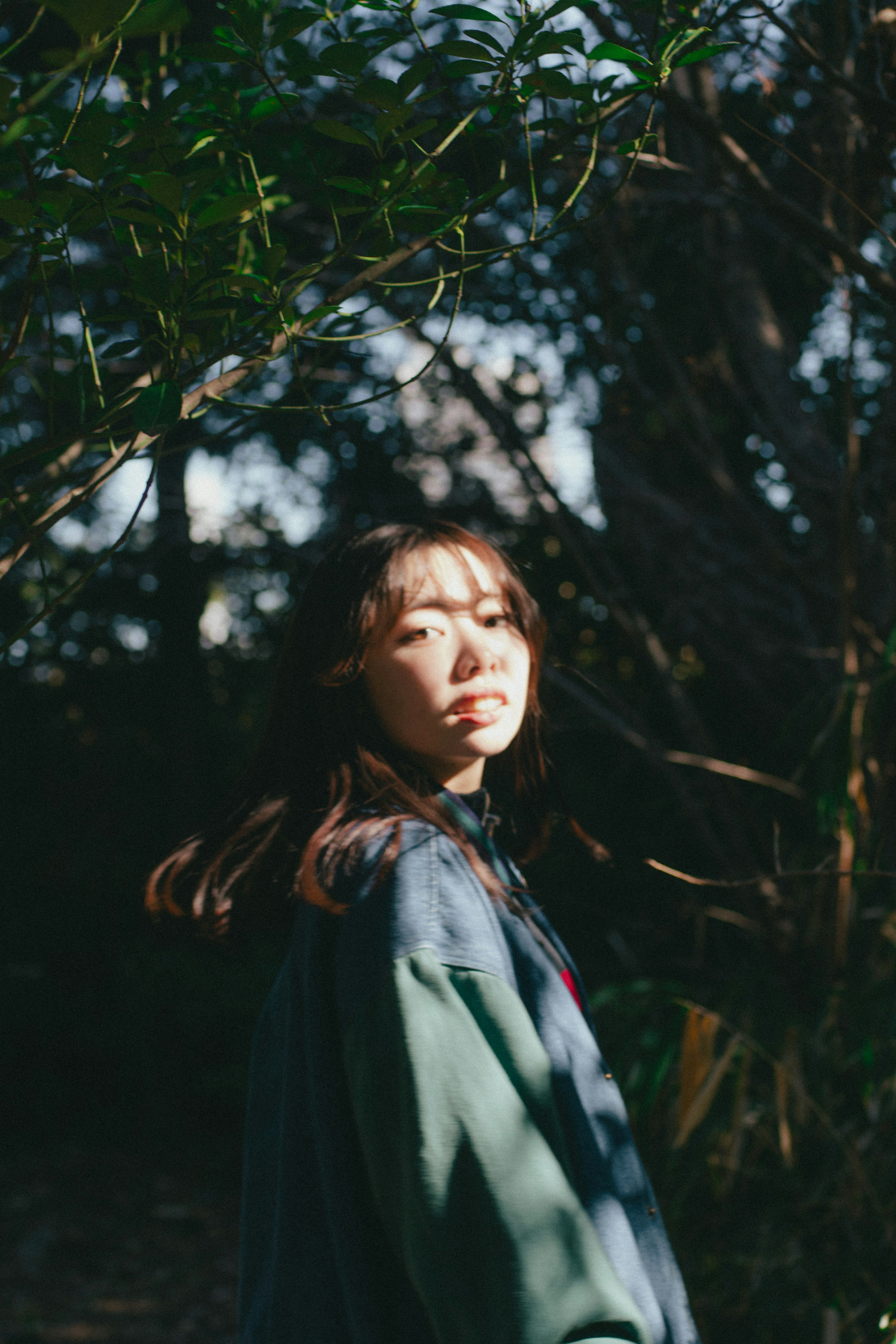 Una mujer con un atuendo verde girándose en un bosque con luz solar filtrando entre los árboles