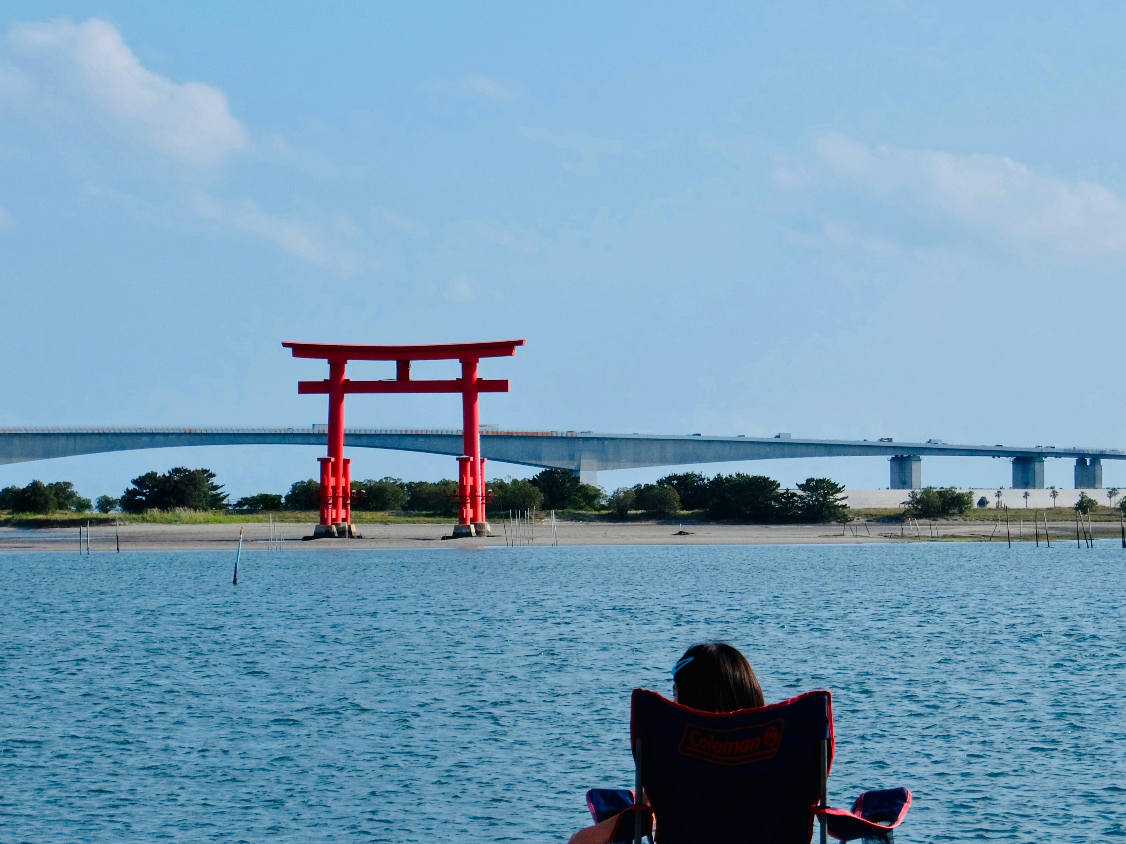 Puerta torii roja con una persona relajándose junto al agua