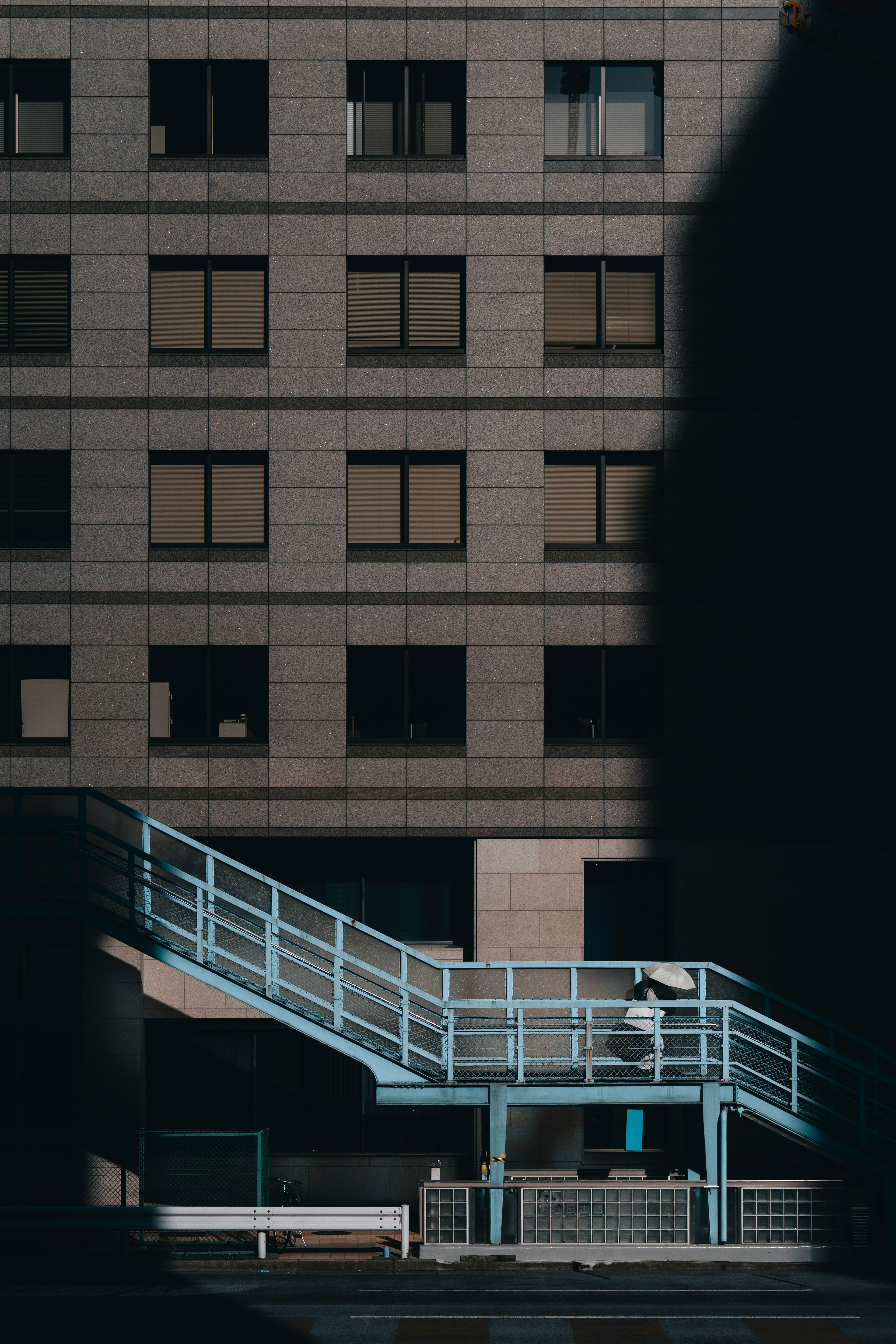 Exterior de un edificio con una escalera azul y contraste de sombras