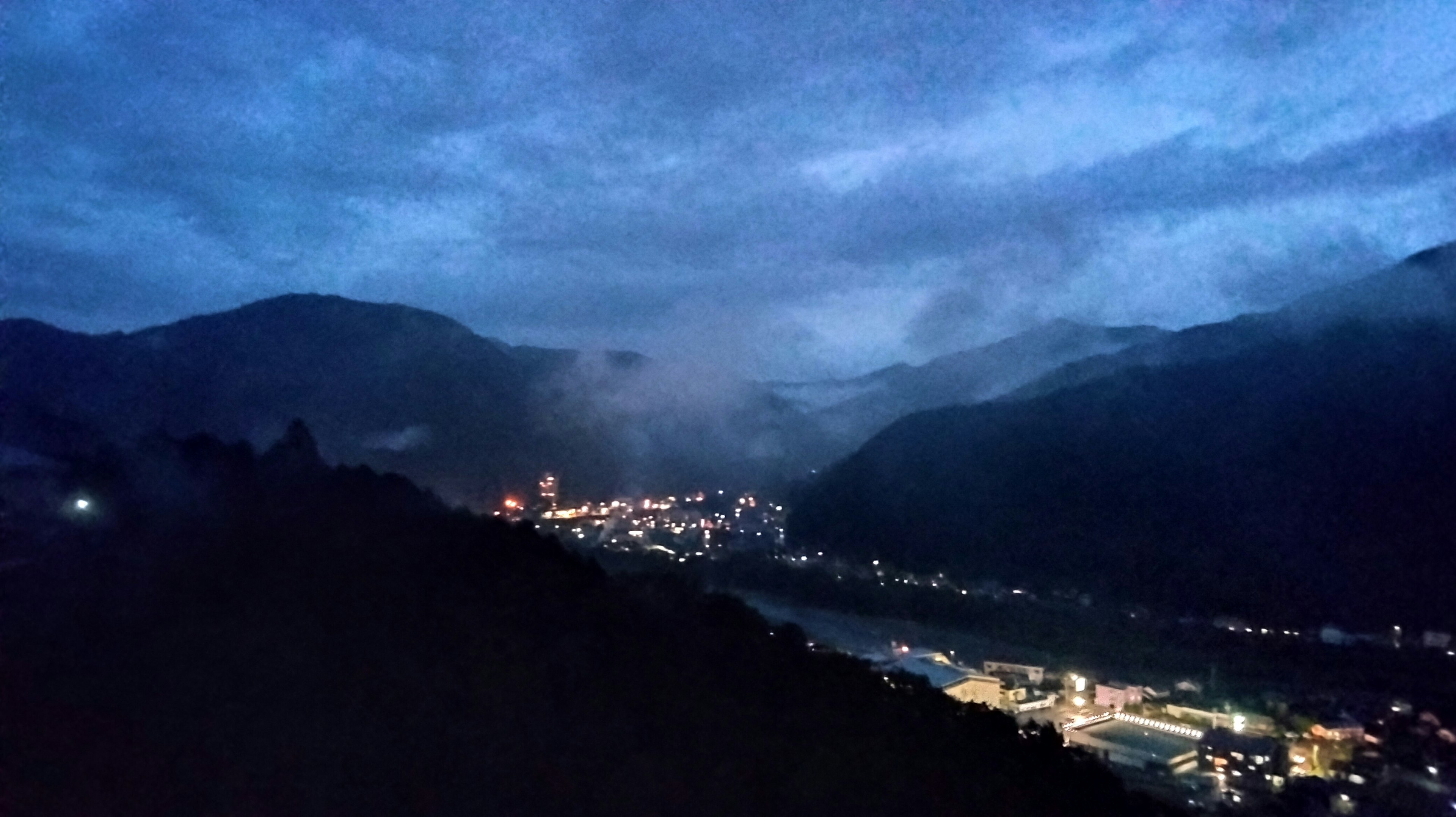 Paesaggio notturno di montagne con luci di città e nebbia