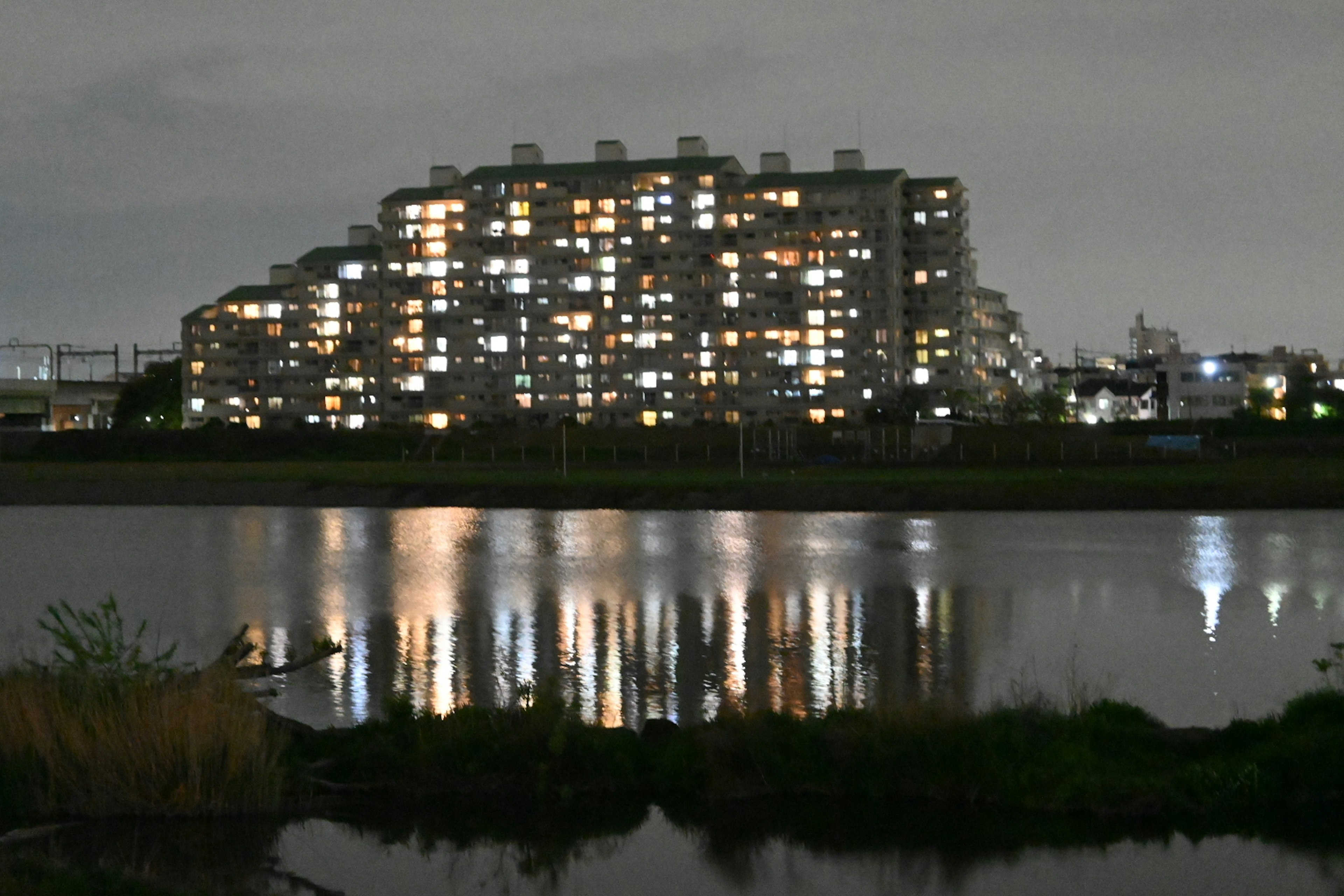 Edificio residenziale con finestre illuminate riflesse nel fiume di notte