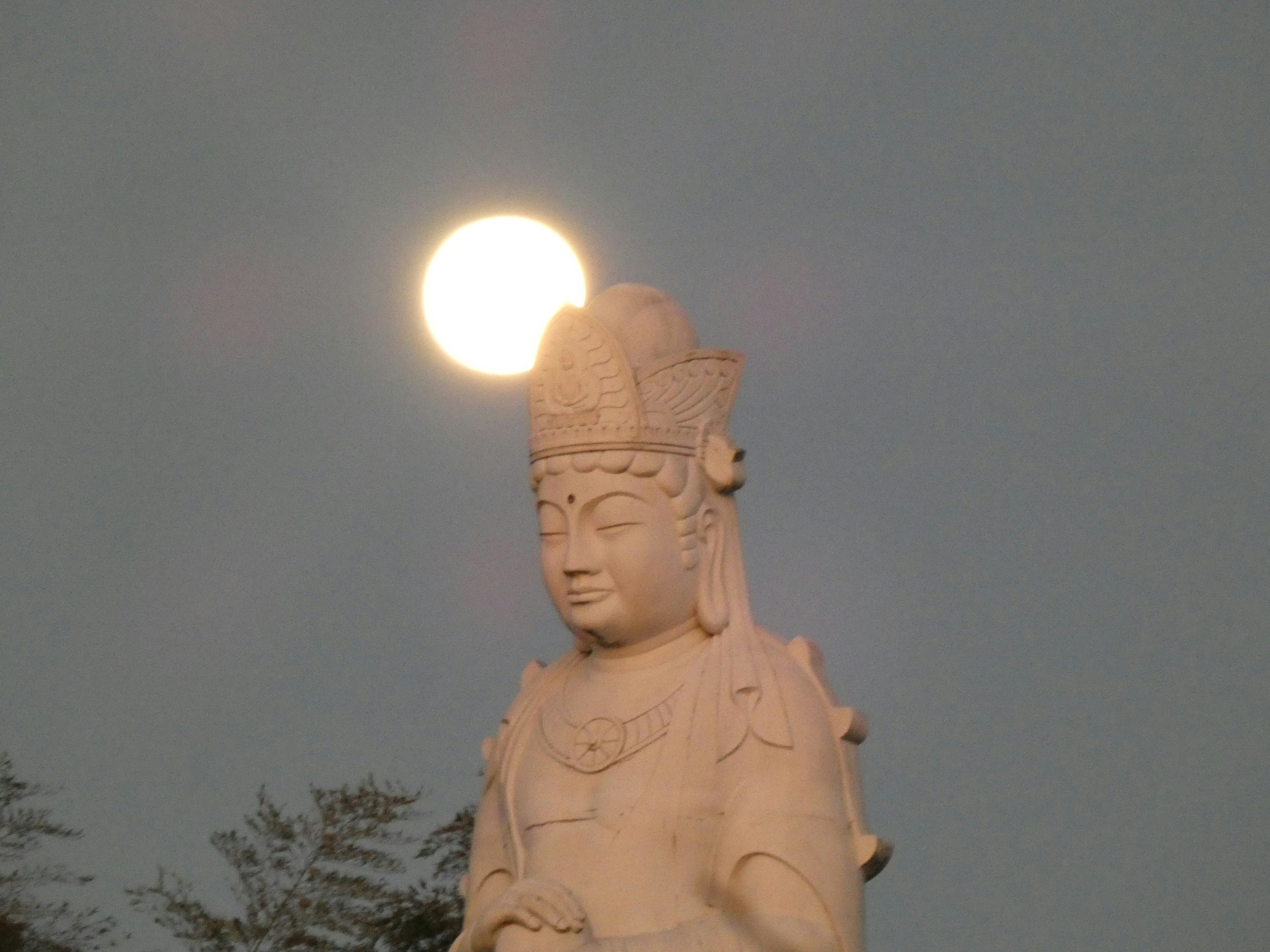 Silhouette of a Kannon statue with the moon above