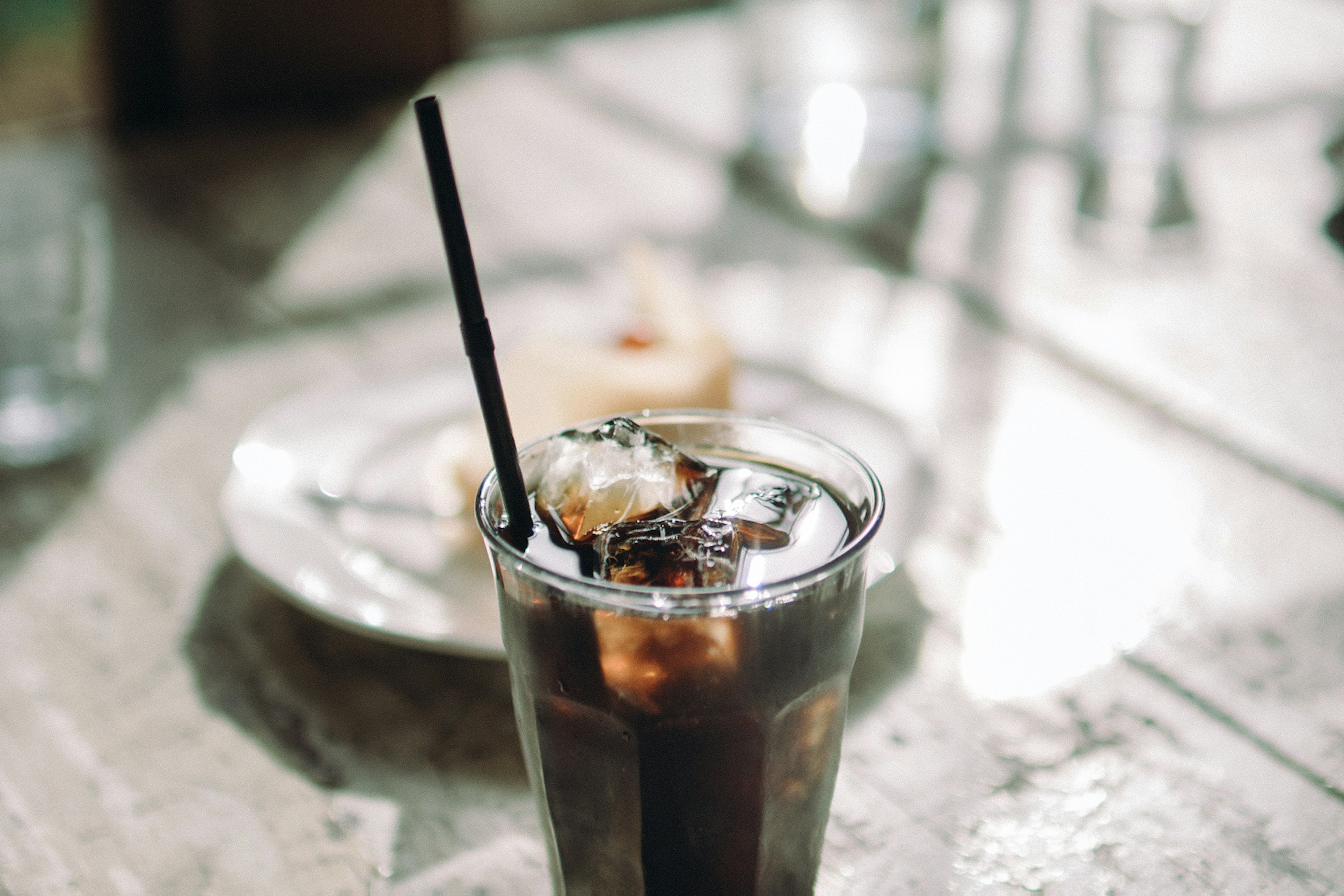 Ein transparentes Glas mit Eiskaffee und Eiswürfeln sowie einem Strohhalm auf einem Tisch