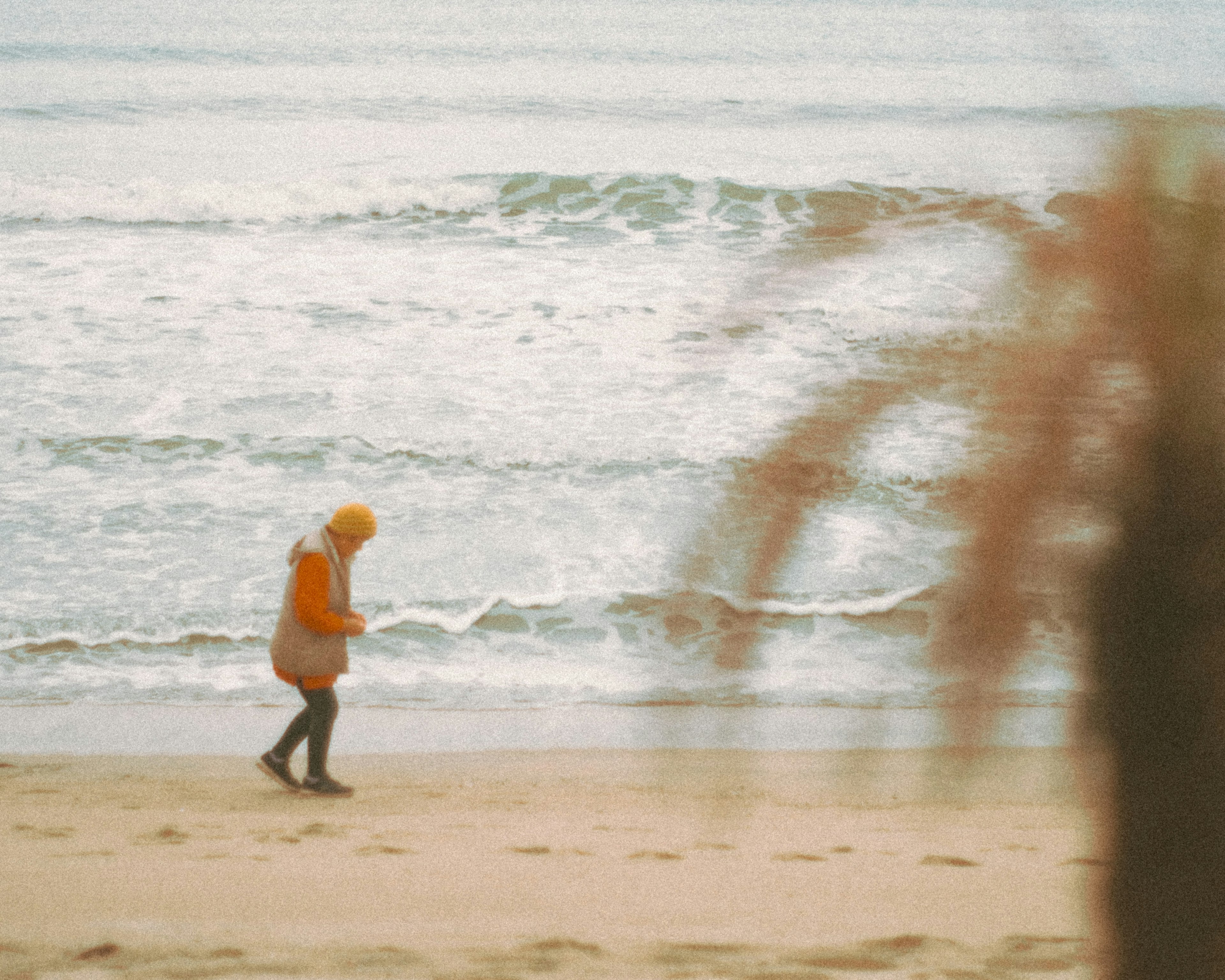 Orang dengan mantel kuning berjalan di pantai dengan ombak