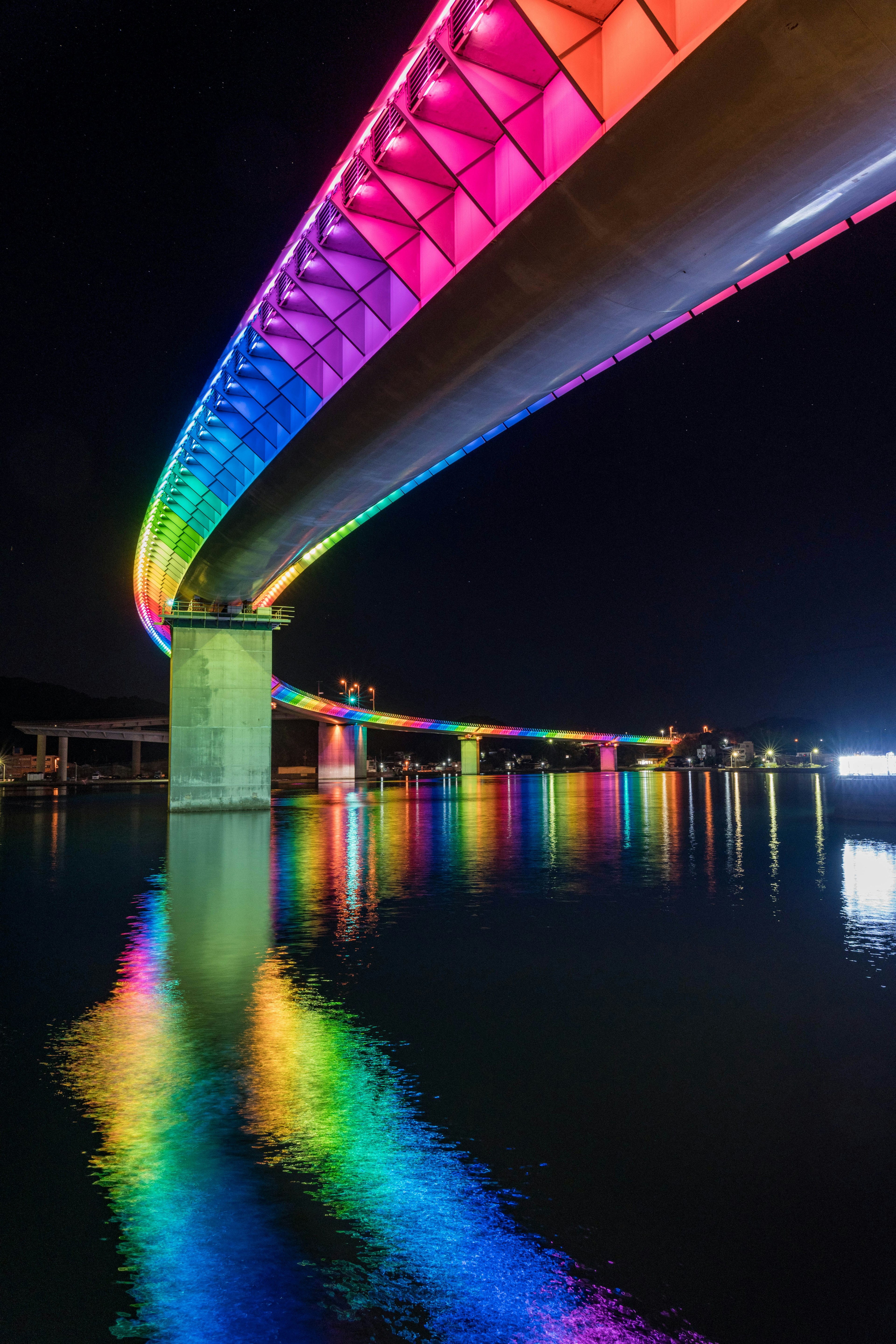 Regenbogenbeleuchtete Brücke bei Nacht, die sich im Wasser spiegelt