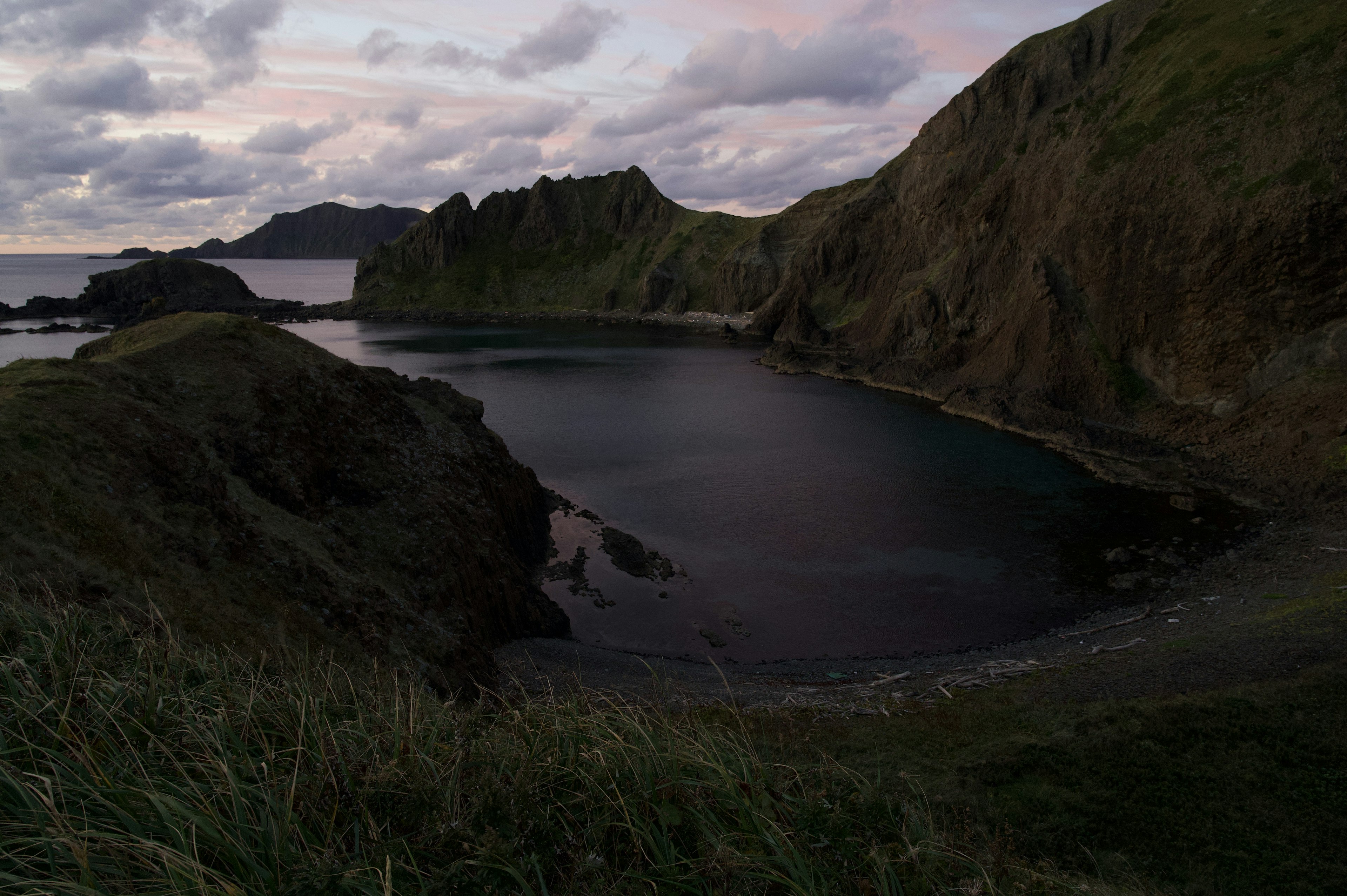 Quiet coastal bay with green hills and dark water surface under twilight sky