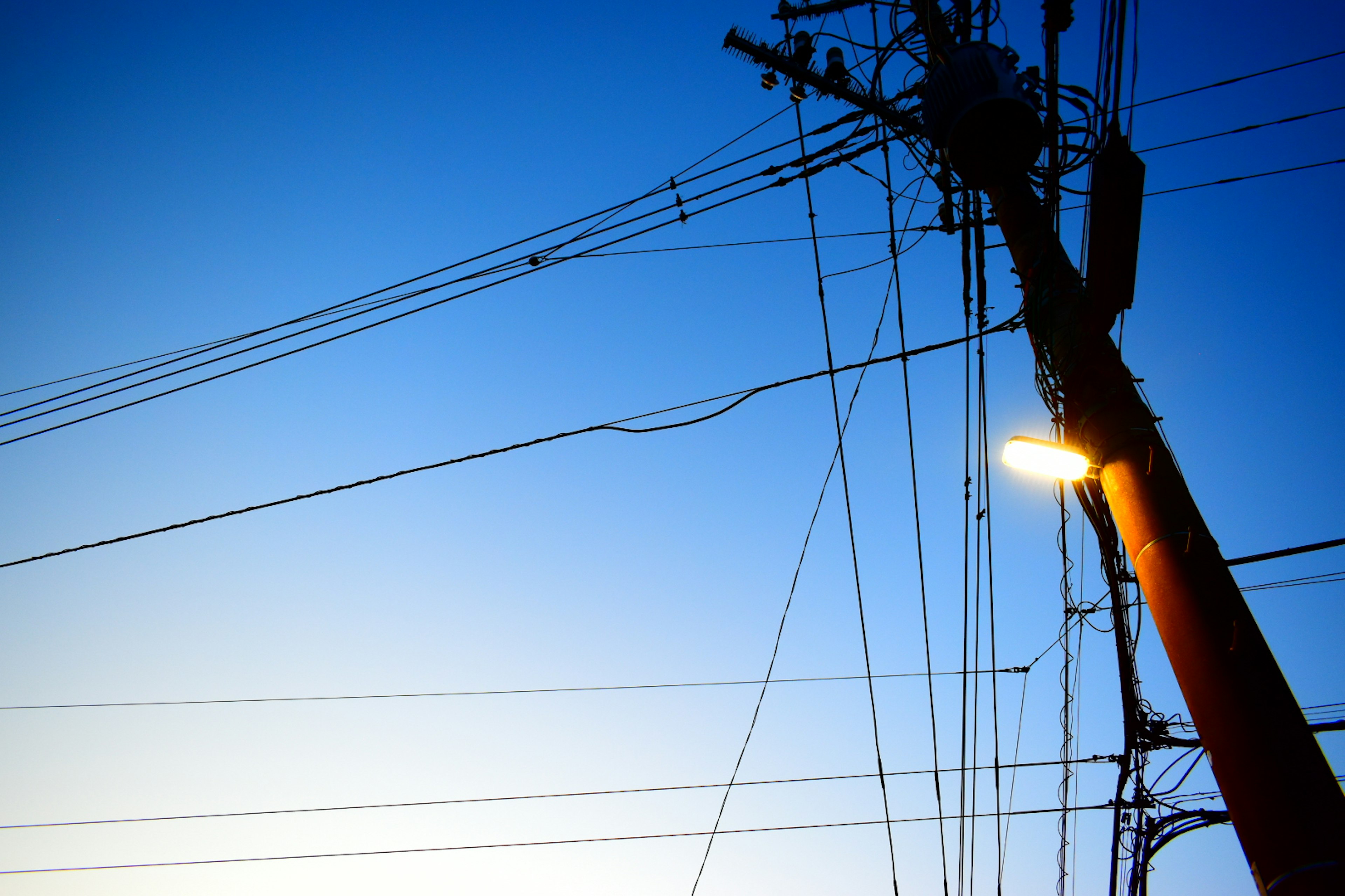 Silhouette of a utility pole and power lines against a blue sky