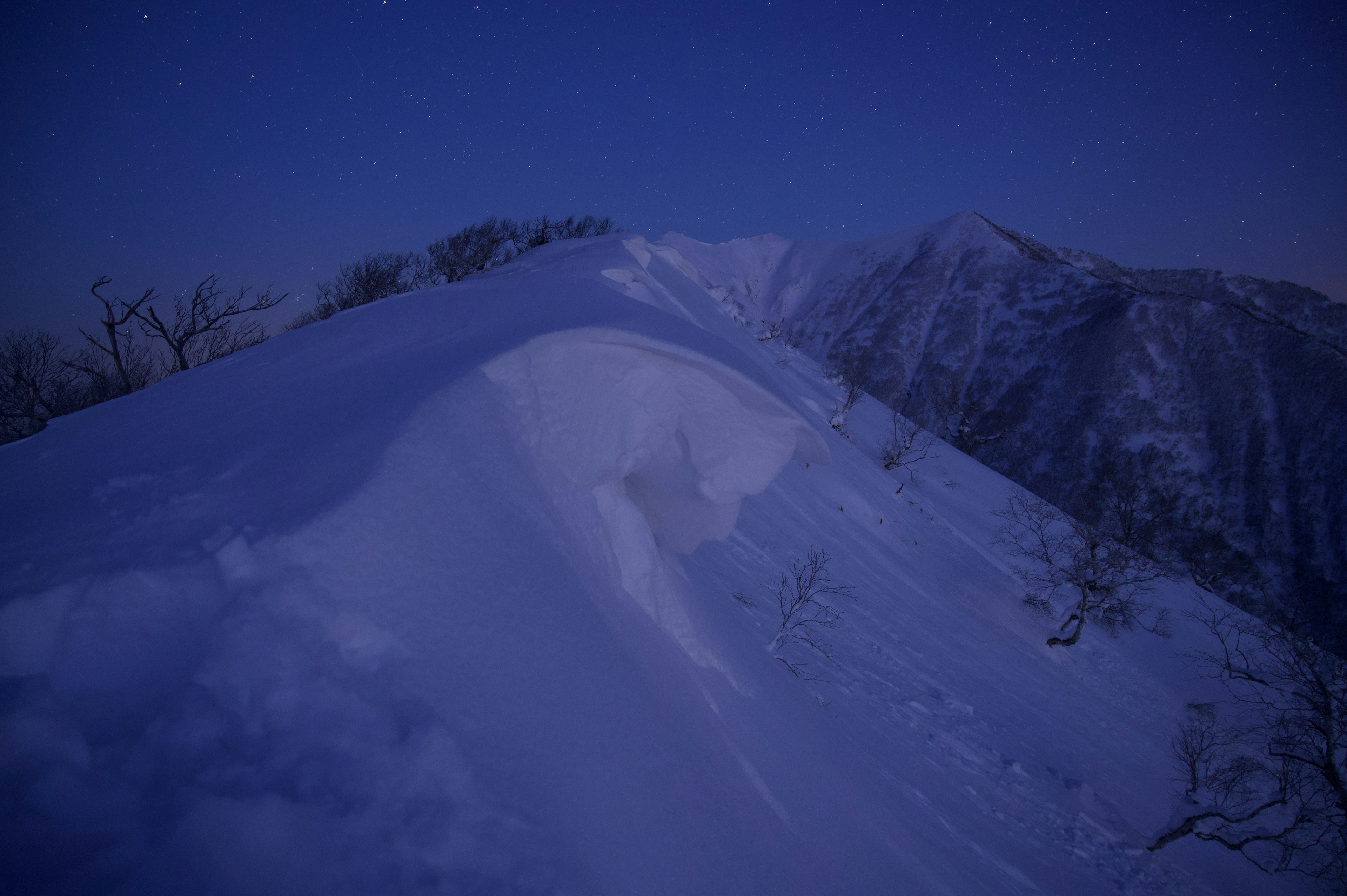 雪に覆われた山の稜線が薄明かりの中に浮かび上がる風景