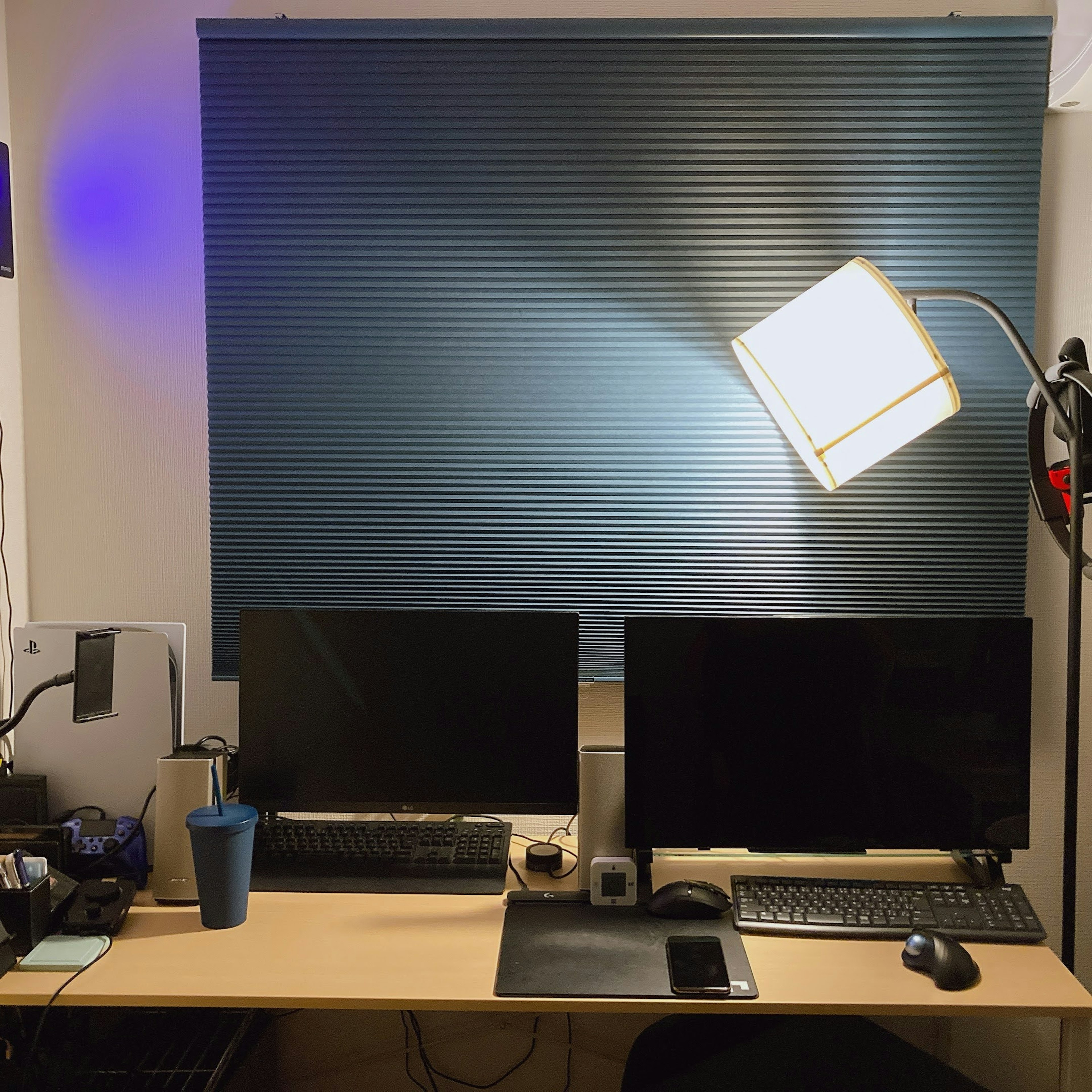 A workspace featuring two monitors on a desk with blue blinds in the background