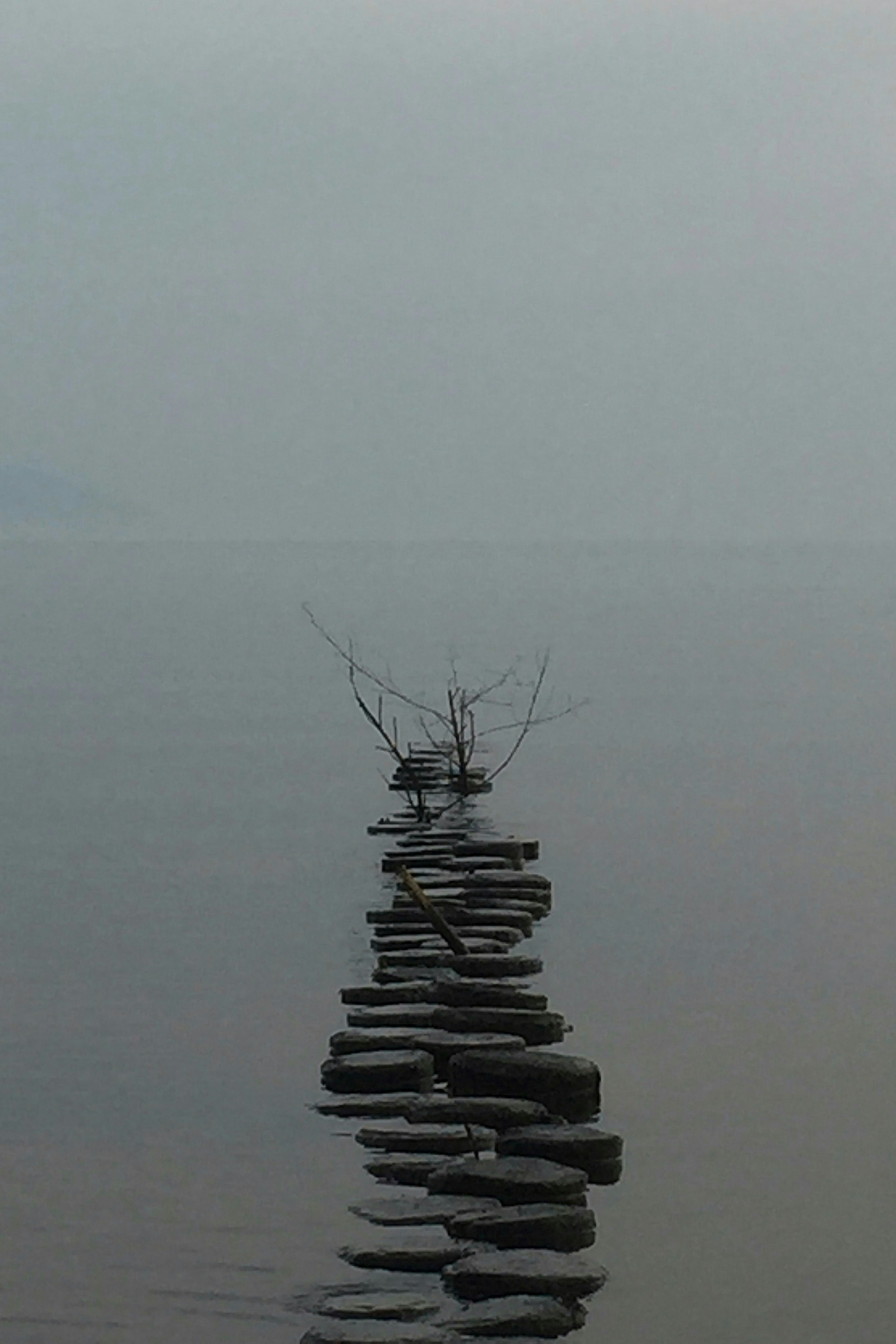 Eine ruhige Landschaft mit einem Steinweg, der aus dem Nebel auftaucht und sich auf der Wasseroberfläche spiegelt