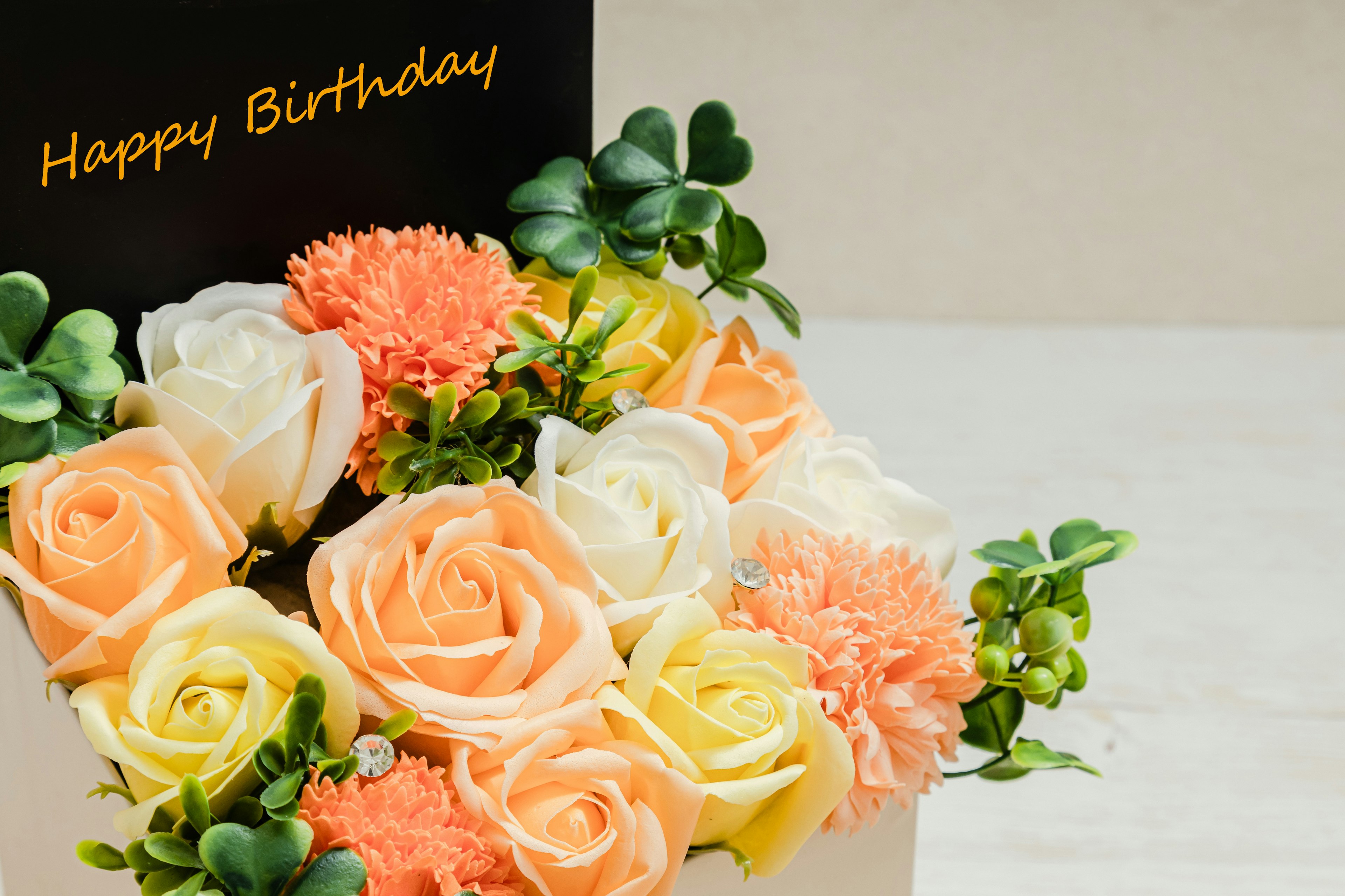 A bouquet of peach and white roses with a black card saying Happy Birthday